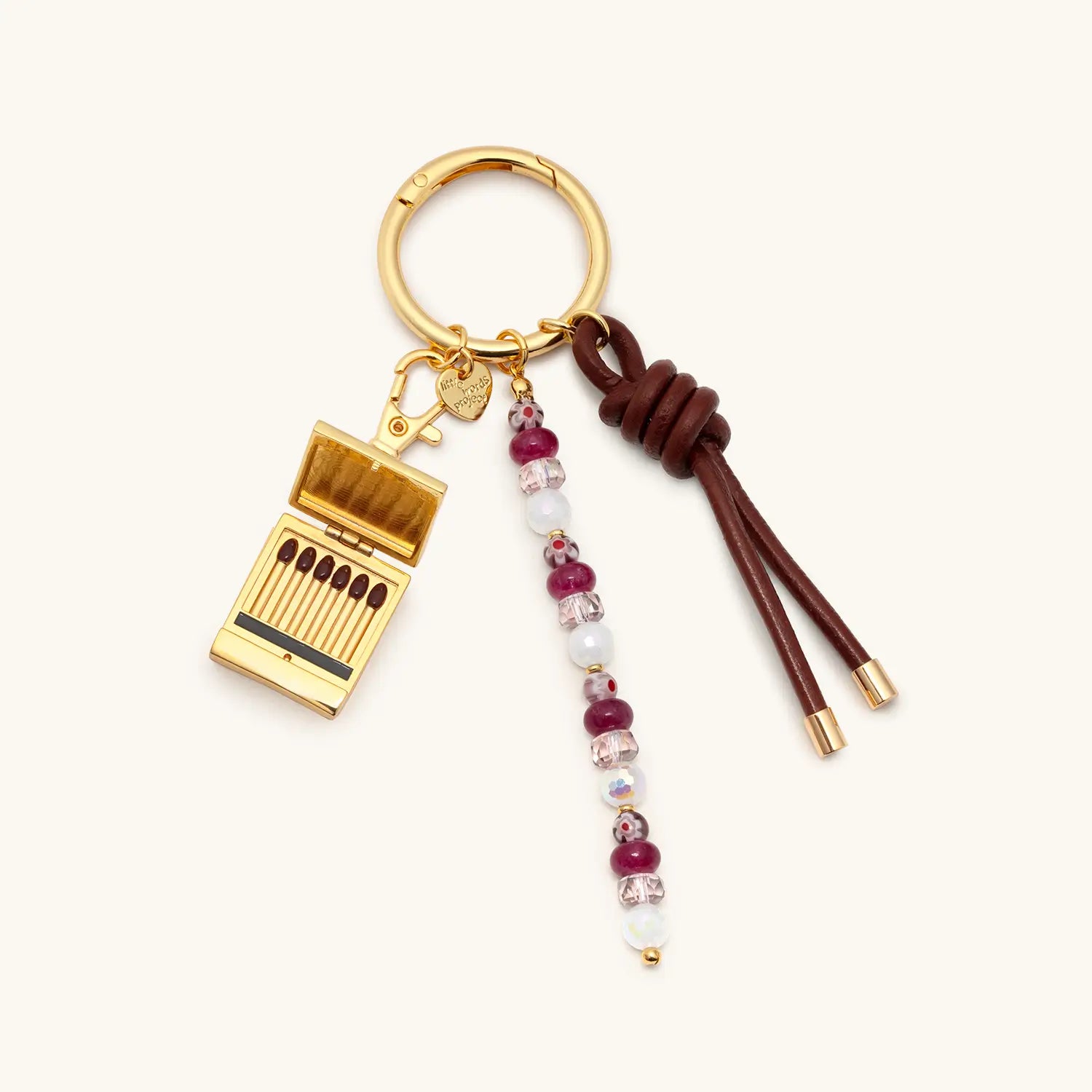 Keychain with gold charm, beads, and leather cord on a white background