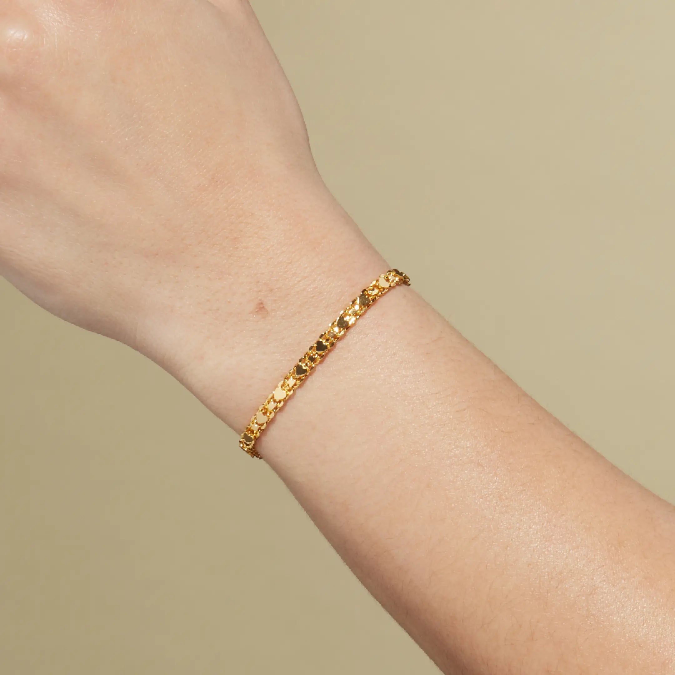 Gold bracelet on a wrist against a beige background