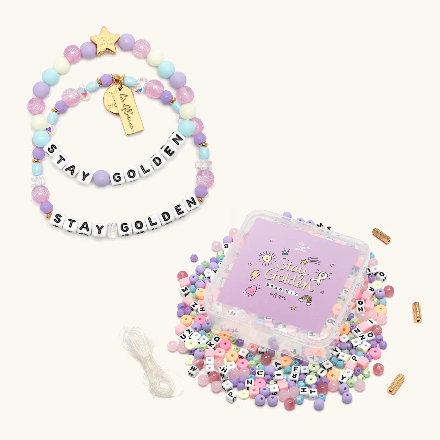 Stay Golden Bead Kit Set Rylee Ta with white letter bead bracelet, kids bracelet and purple bead kit box with loose pastel beads, flat lay on cream background