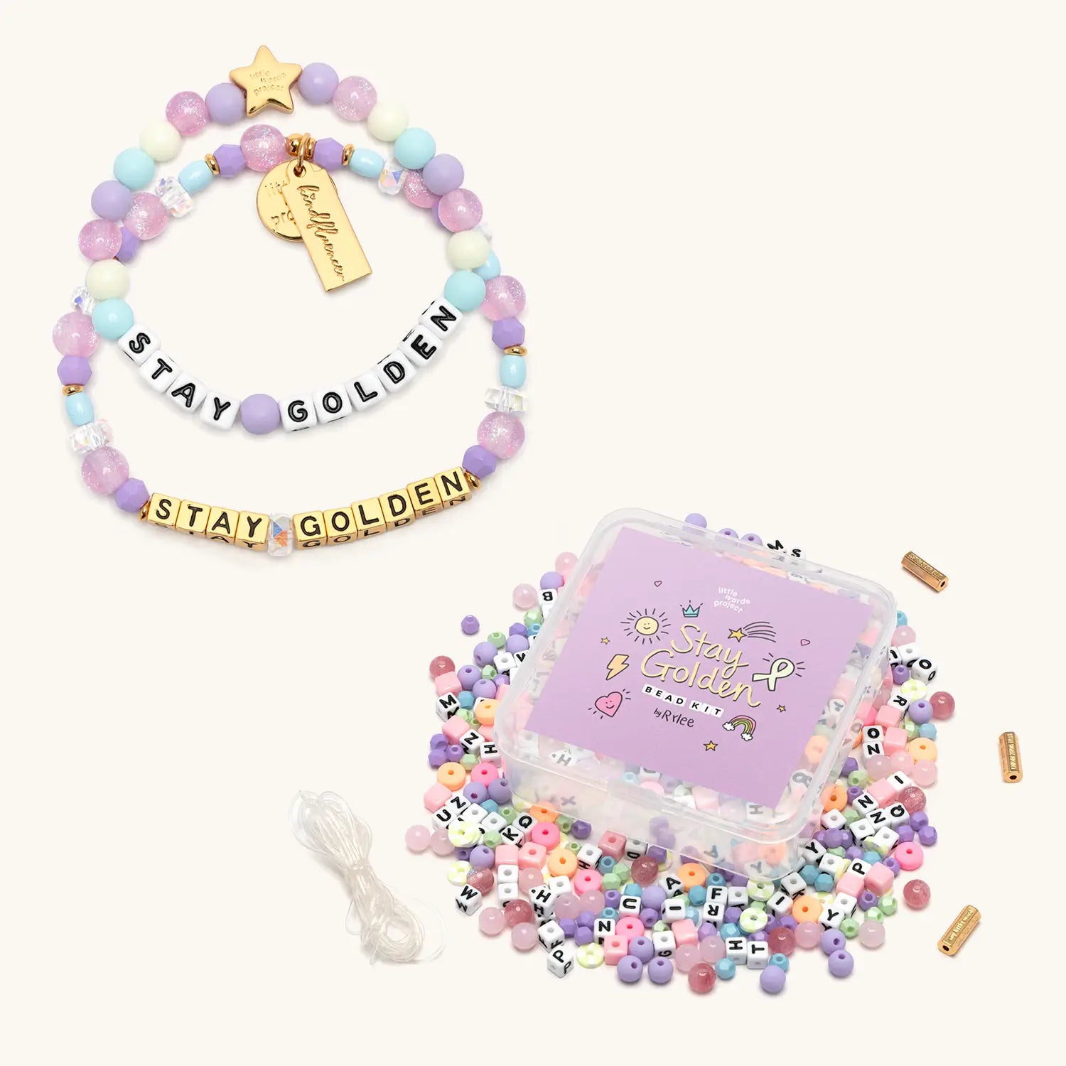 Stay Golden Bead Kit Set Rylee Ta with gold letter bead bracelet, kids bracelet and purple bead kit box with loose pastel beads, flat lay on cream background