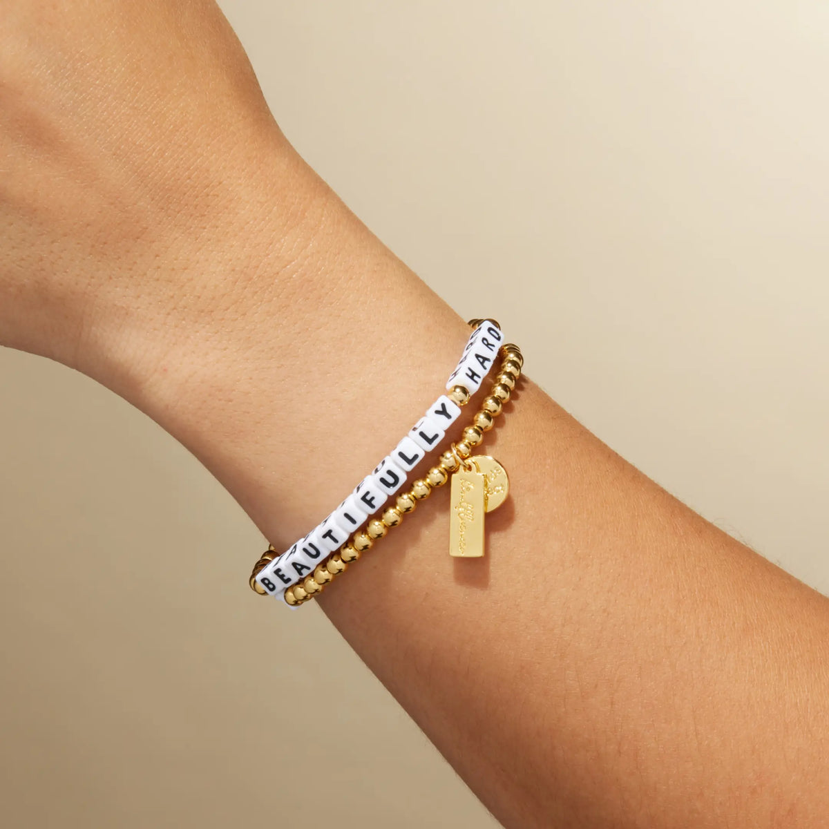 Beautifully Hard bracelet by Kirstin Czernek on-model on wrist, white letter beads with gold plated beads and gold accents