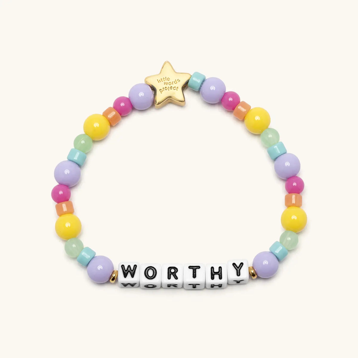 Worthy kids bracelet by Kirstin Czernek, white letter beads with pink, yellow, lavender, mint, and aqua beads and a gold star bead, flat-lay on cream background
