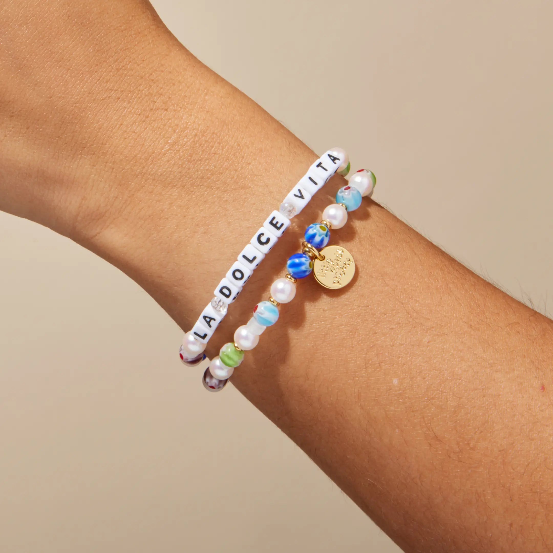 Bracelet with colorful beads and a gold tag on a wrist against a beige background