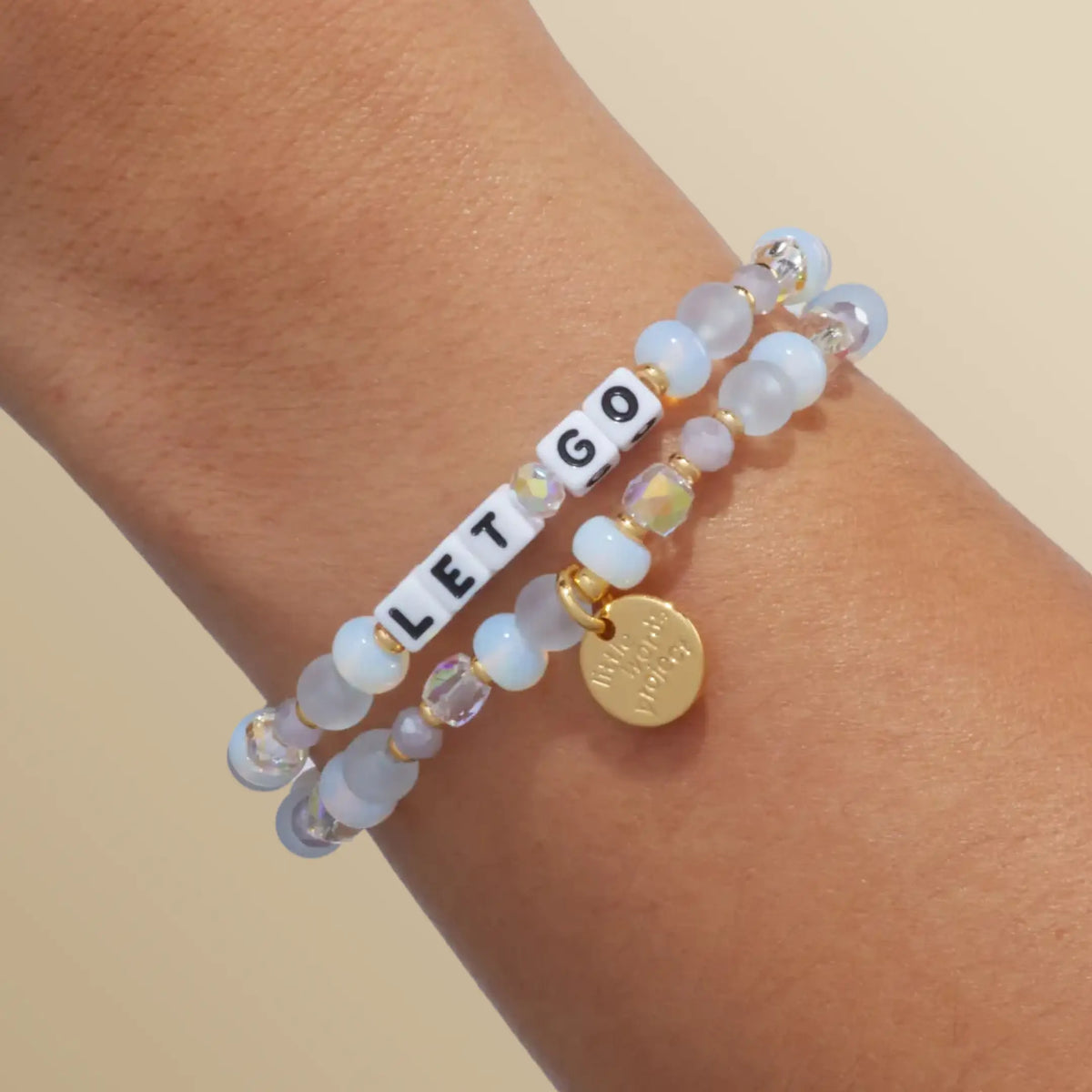 Let Go bracelet in the Marshmellow bead pattern with white letter beads, stacked with a second bracelet, on-model wrist shot on warm neutral background