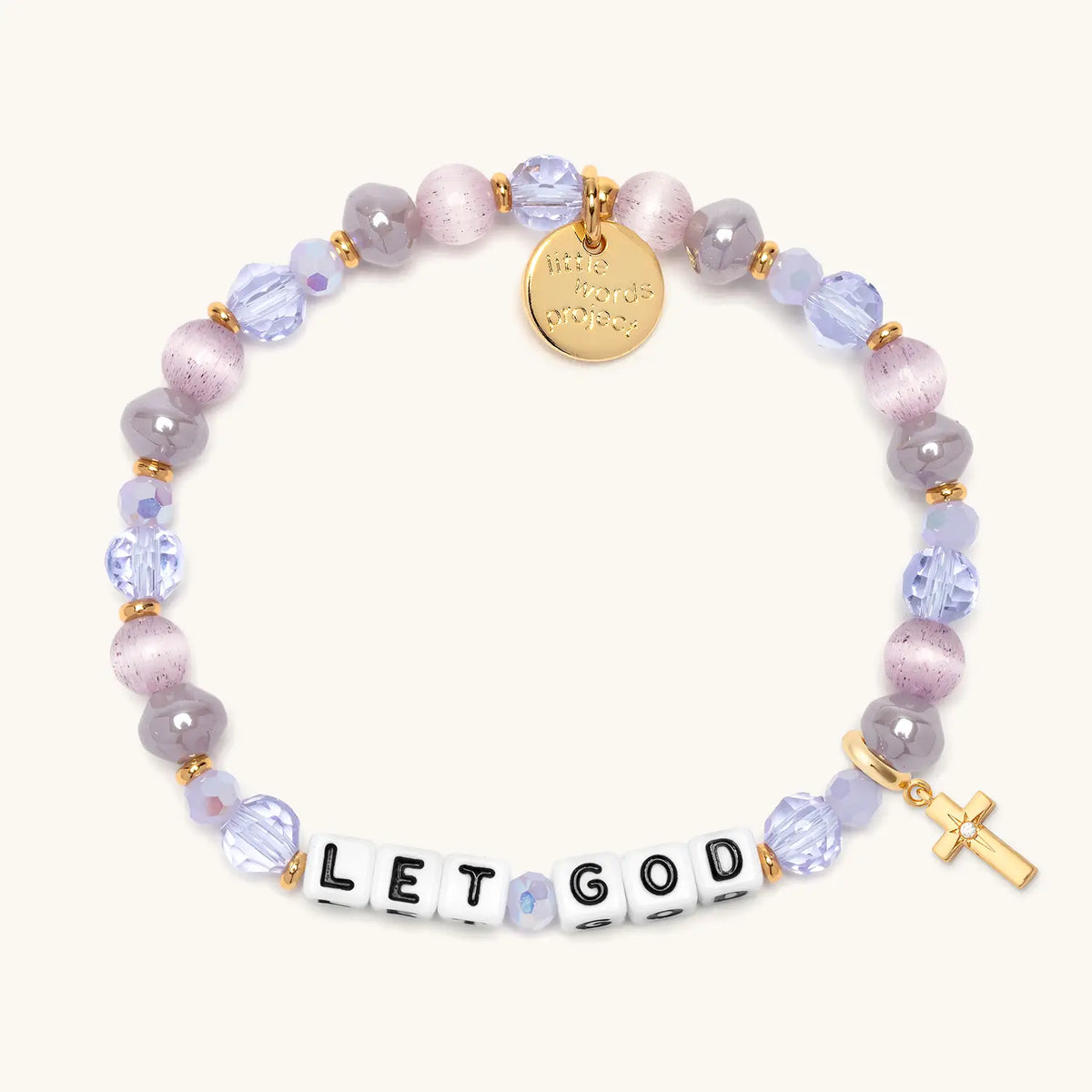 Let God bracelet in the Purple Twinkle bead pattern with white letter beads, gold puffy cross charm with a clear CZ stone, flat-lay on cream background