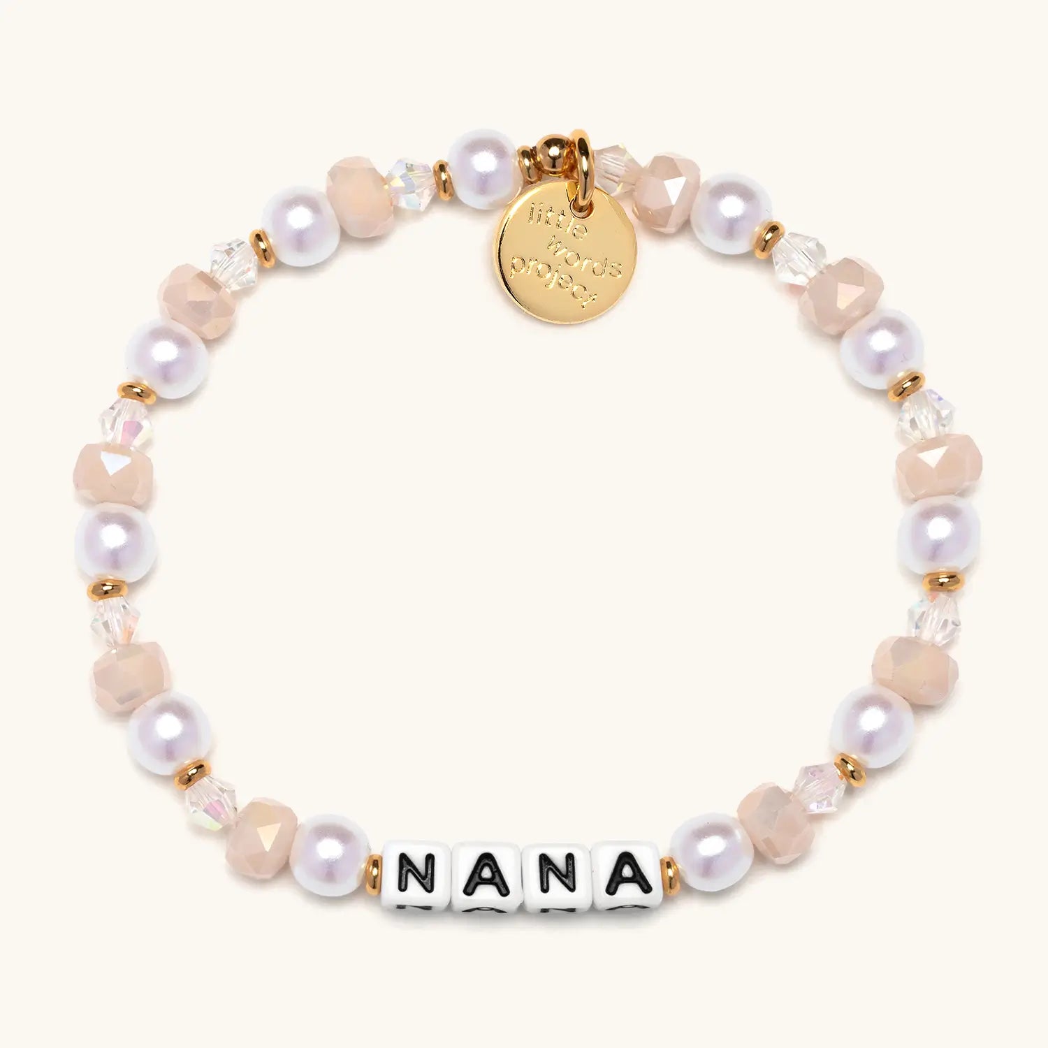 A beaded bracelet spelling "NANA" in white square letter beads with black lettering, accented with pink faceted crystal beads, white pearl beads, clear crystals, and gold spacer beads. A small gold circular charm hangs from the top of the bracelet.