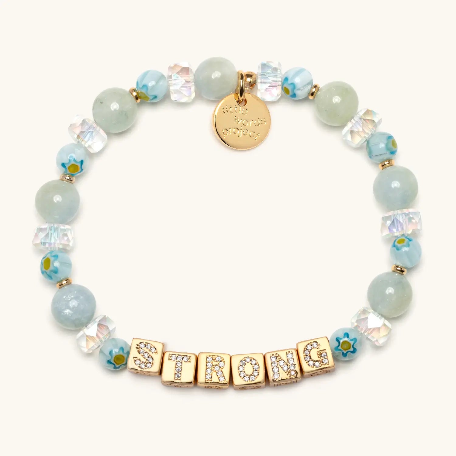 Beaded bracelet arranged in a circle, featuring pale green and light blue round beads, faceted clear spacers, and small blue floral accents, with gold cube beads spelling “STRONG” and a small round gold charm on a neutral background.