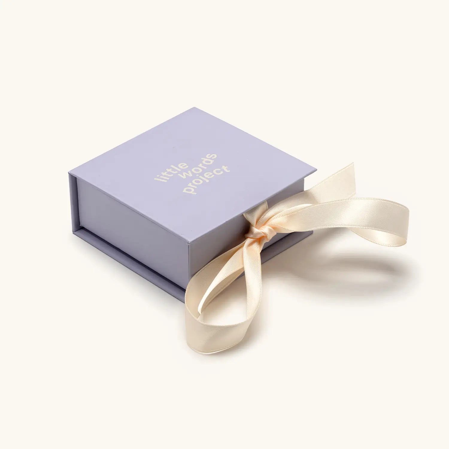A small square lavender gift box with "little words project" printed in white text on the lid, tied with a cream satin ribbon bow.