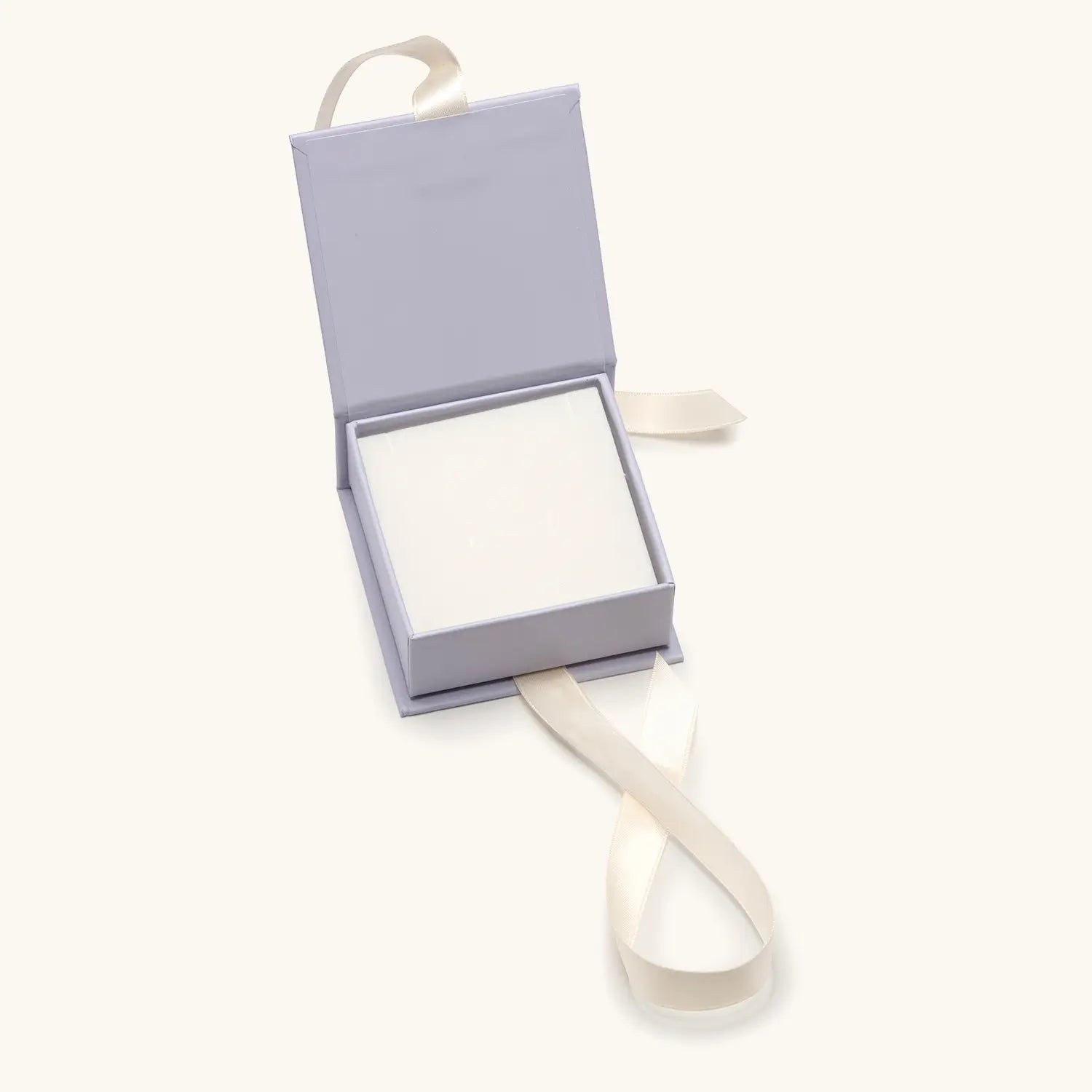 An open small square lavender gift box with a white cushioned interior insert, with a cream satin ribbon threaded through the sides.
