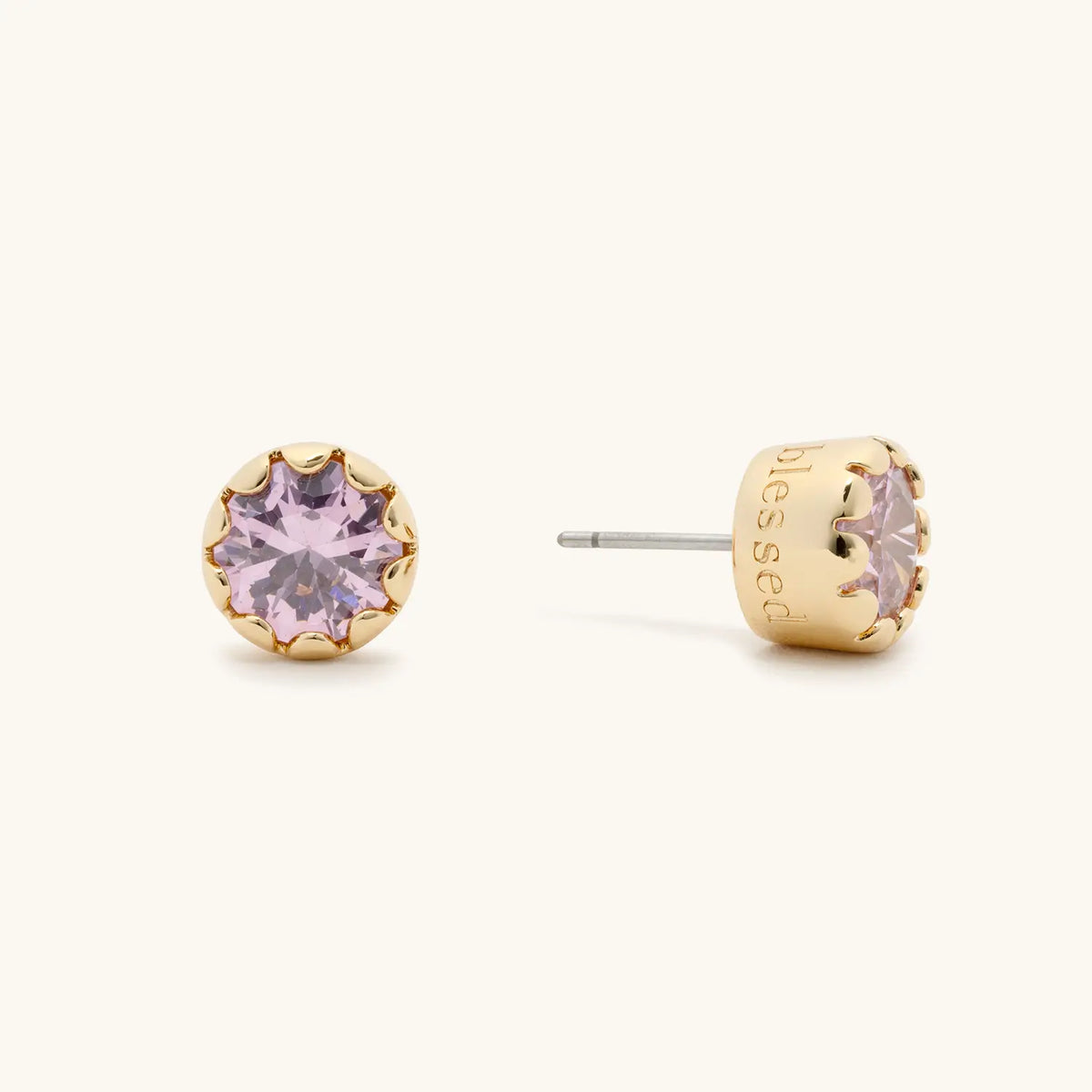 Blessed Scalloped Bezel Studs, 18k gold-plated studs with a pink CZ stone in a scalloped bezel and blessed engraved on the side, flat-lay on cream background