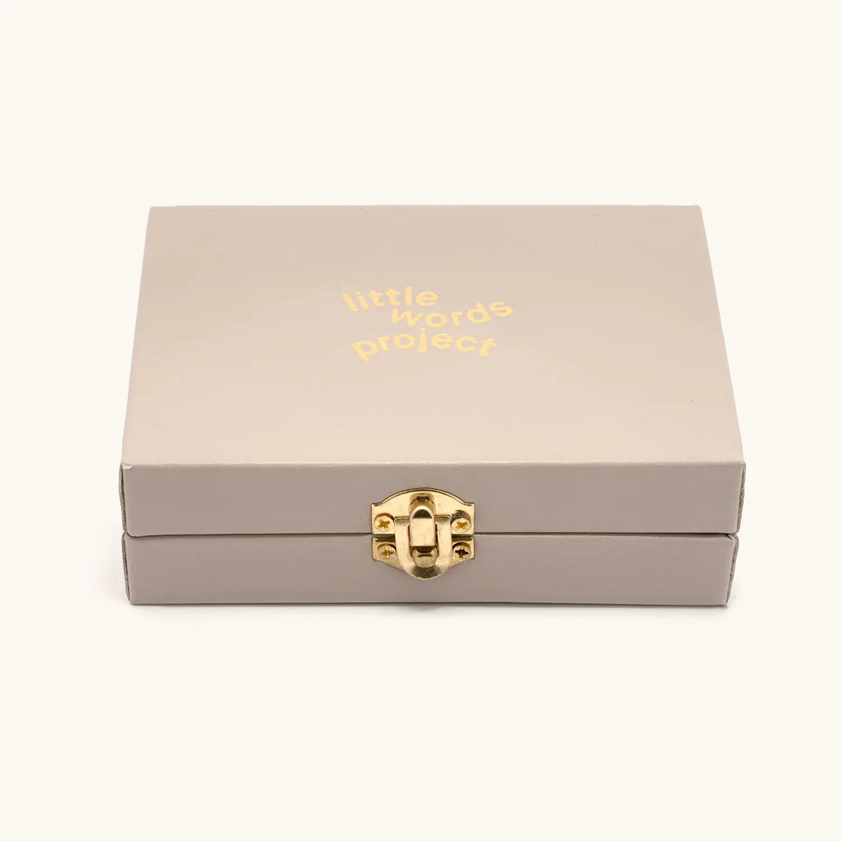 Lariat Charm Set limited edition trunk box, taupe box with gold Little Words Project logo and gold latch, front view packaging shot on cream background
