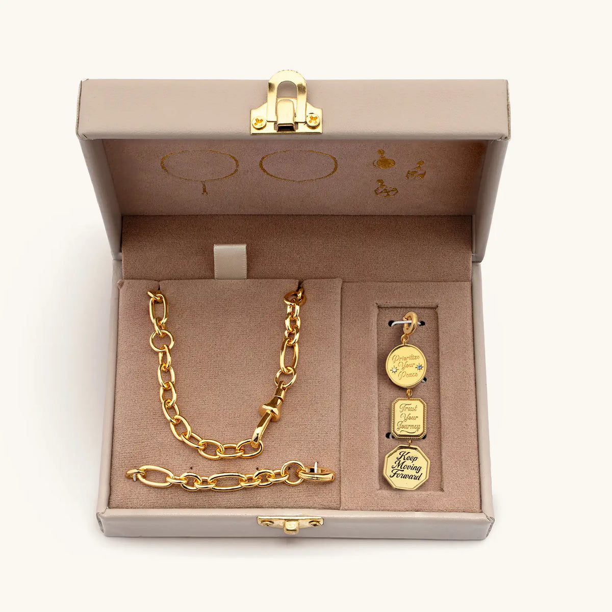 Lariat Charm Set open trunk box with the gold lariat necklace and the Prioritize Your Peace, Trust Your Journey, and Keep Moving Forward charms, packaging shot on cream background