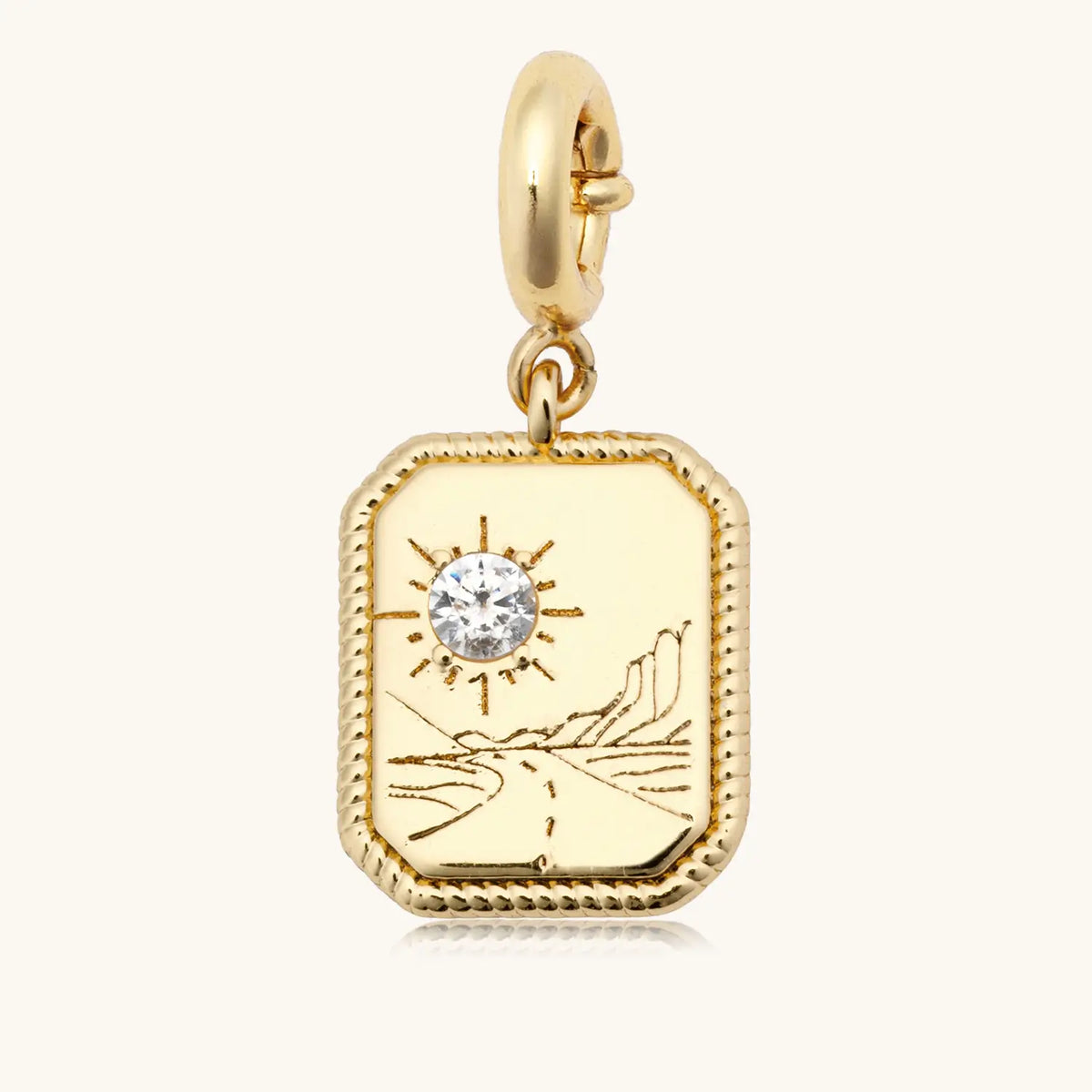 Trust Your Journey Charm back, 18k gold-plated rectangular medallion with a CZ sun rising over a winding road and mountains on a gold spring ring clasp, detail on cream background