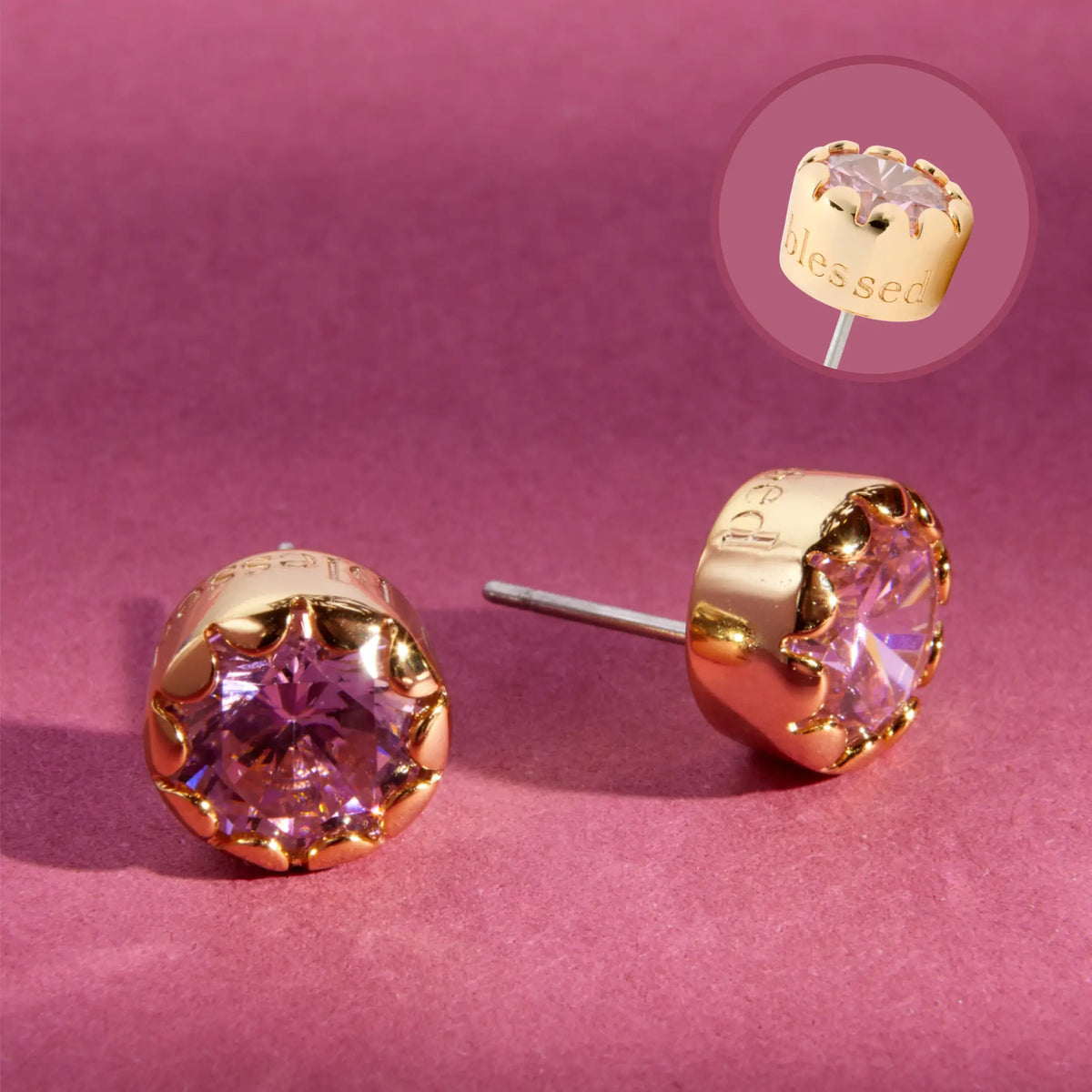 Blessed Scalloped Bezel Studs, 18k gold-plated studs with a pink CZ stone in a scalloped bezel, with an inset showing blessed engraved on the side, detail on a berry background