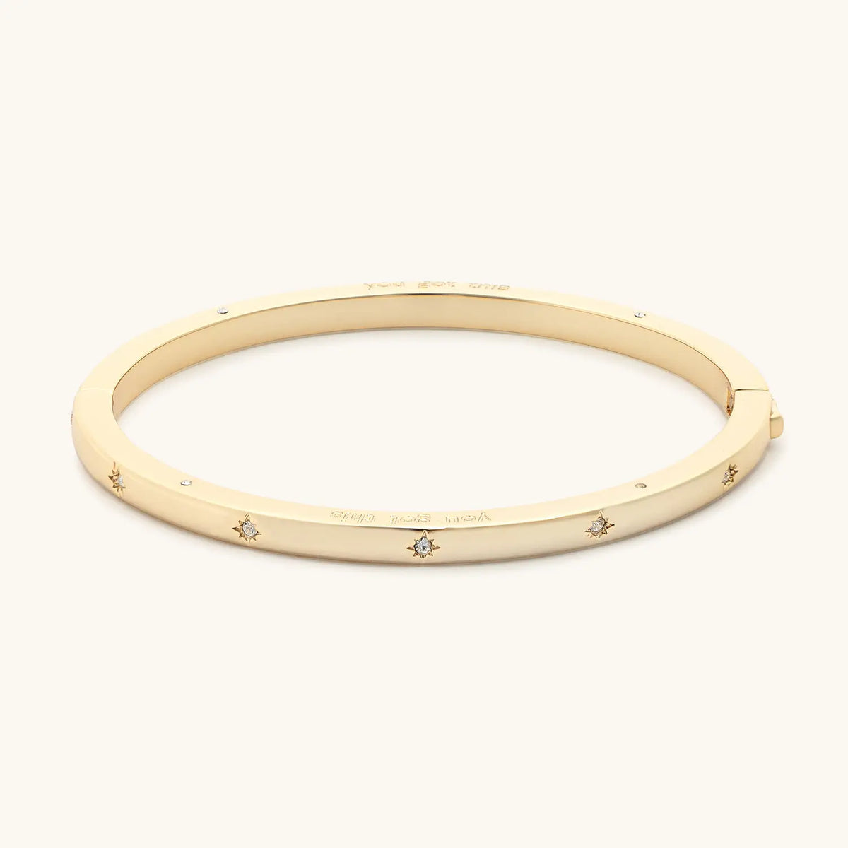 You Got This Bangle side view, 18k gold-plated bangle with starburst CZ stone details along the outside, detail on cream background