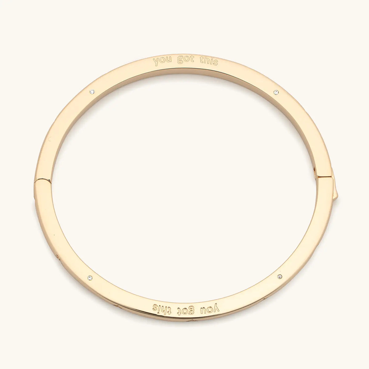 You Got This Bangle, 18k gold-plated bangle engraved you got this with CZ stone details and push button closure, flat-lay on cream background