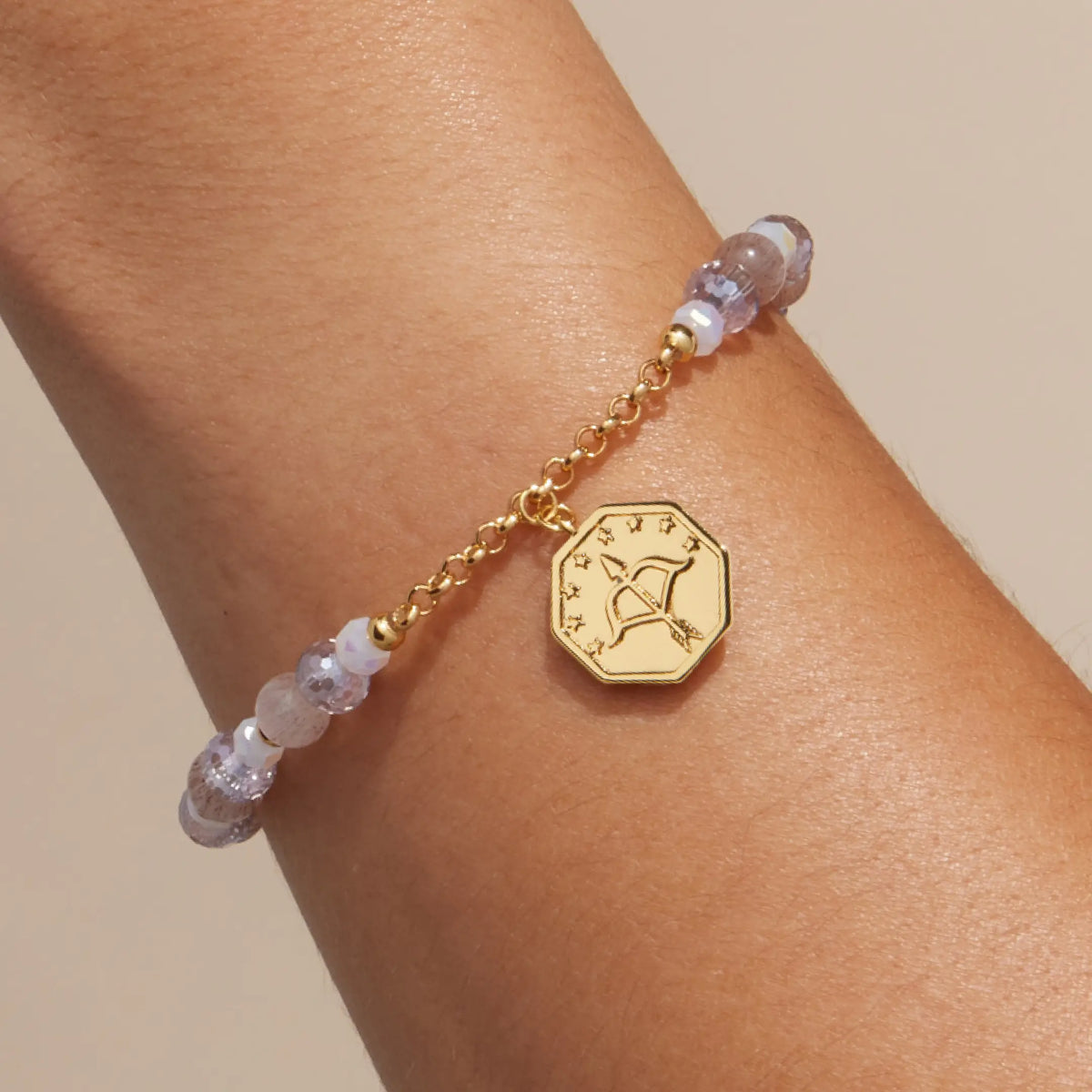 Keep Moving Forward Charm Bracelet on-model, lilac crystal and pink cat eye beads with gold chain and the bow and arrow side of the octagon medallion facing out