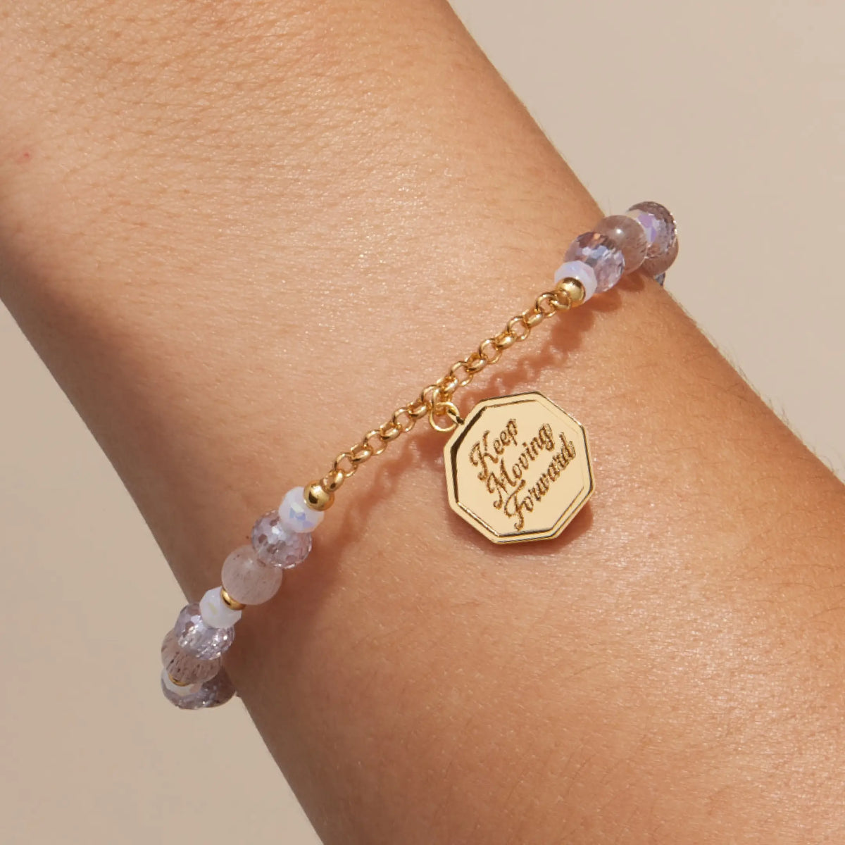 Keep Moving Forward Charm Bracelet on-model, lilac crystal, pink cat eye, and white glass beads with gold chain and the octagon medallion engraved Keep Moving Forward