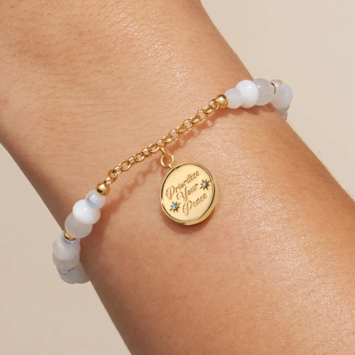 Prioritize Your Peace Charm Bracelet on-model, white cat eye and iridescent crystal beads with gold chain and the round medallion engraved Prioritize Your Peace