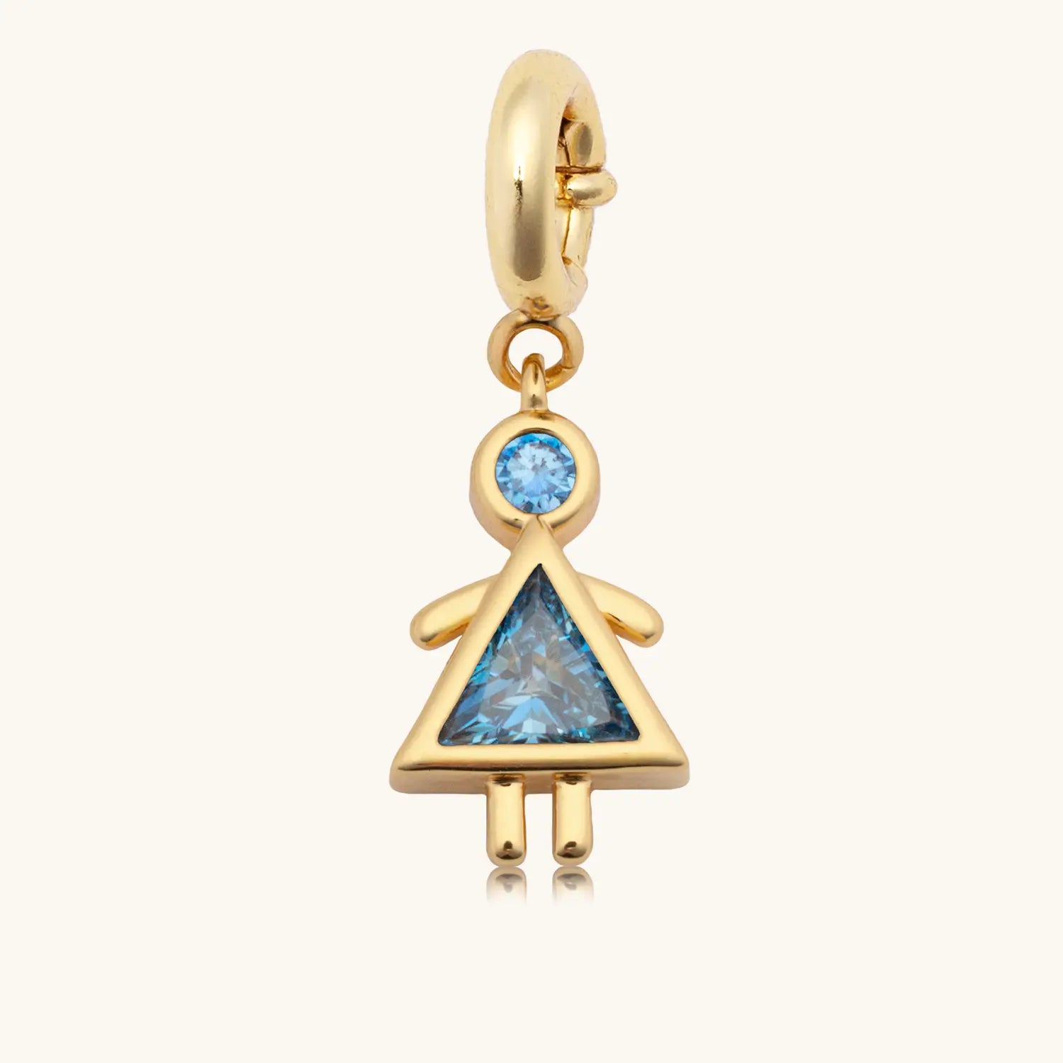 A gold dangle charm in the shape of a girl figure, featuring a round blue gemstone as the head and a triangular blue gemstone as the body forming a dress silhouette, with gold arms and legs, attached to a gold spring-ring clasp.