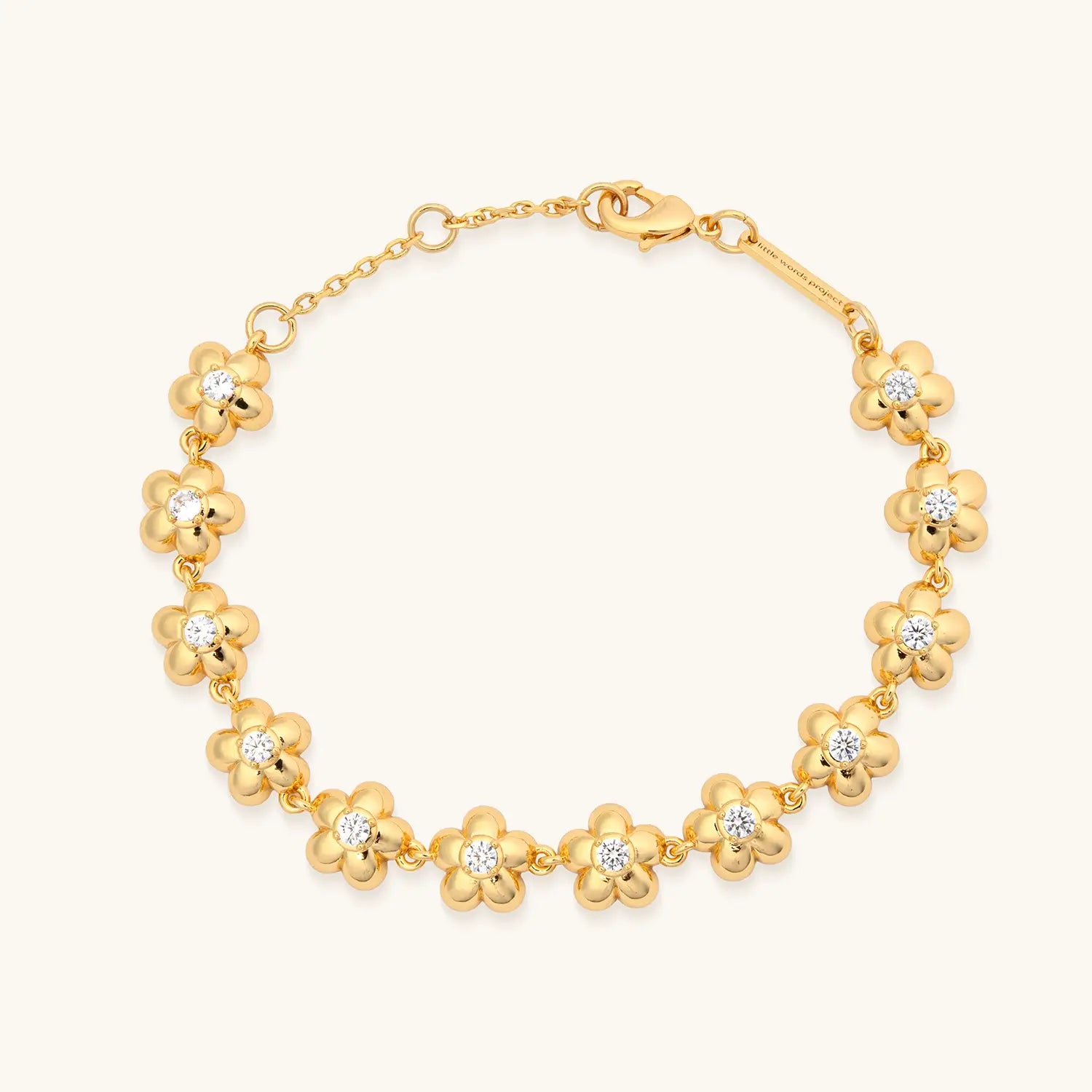 A gold chain bracelet featuring a continuous row of puffy five-petal flower links, each set with a single round clear crystal or diamond at the center. The bracelet fastens with a lobster clasp and includes an adjustable extension chain. Photographed on a warm white background.