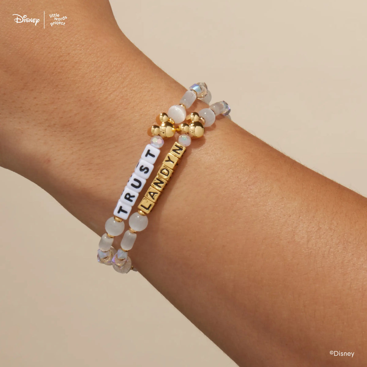 Mickey Custom Magic Maker Disney Mickey & Friends custom bracelets on wrist, one with white letter beads and one with gold letter beads, white cat's eye and iridescent crystal beads with gold plated Mickey Mouse beads