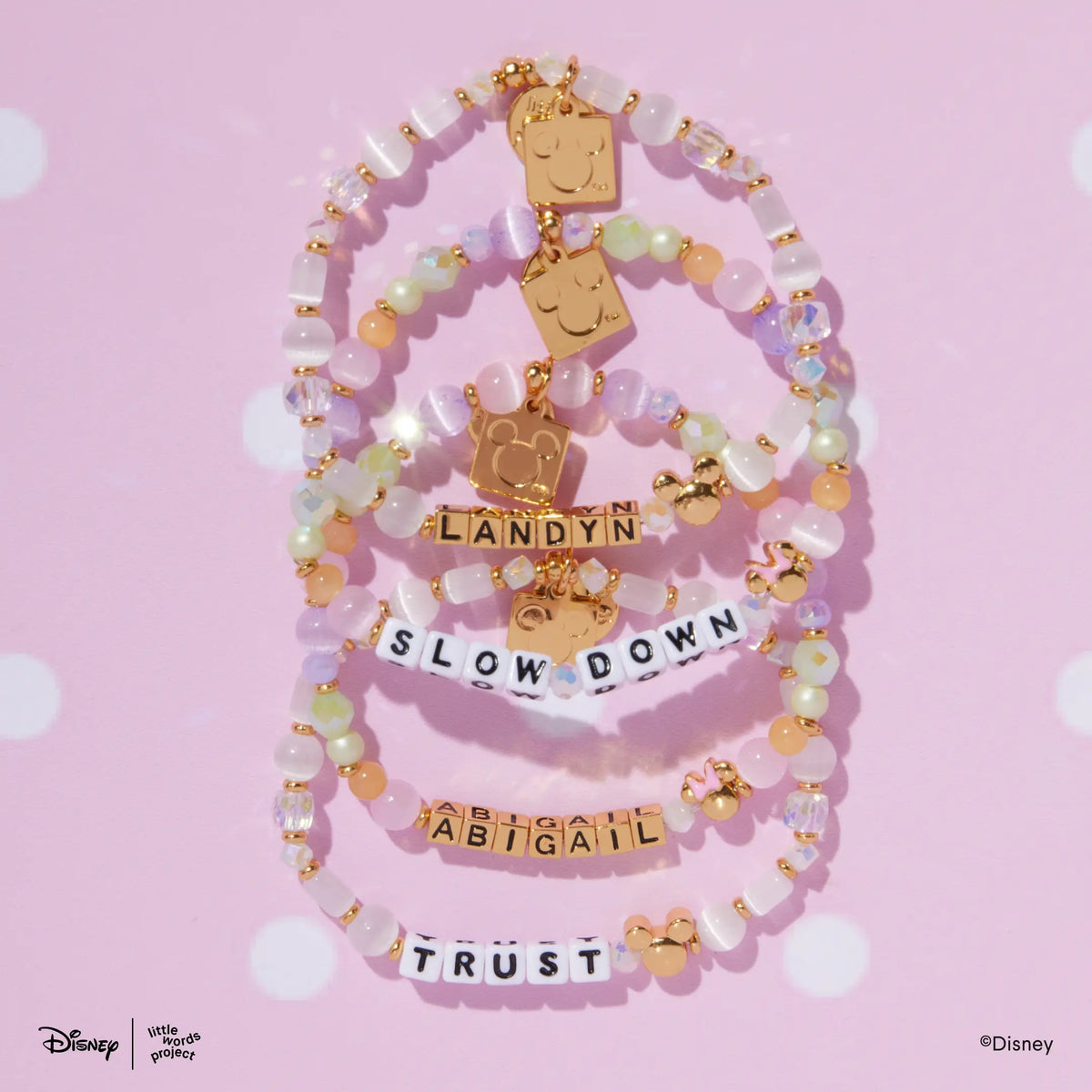 Mickey Custom Magic Maker and Minnie Custom Dot Darling Disney Mickey & Friends custom bracelets stacked, flat lay on pink polka dot background