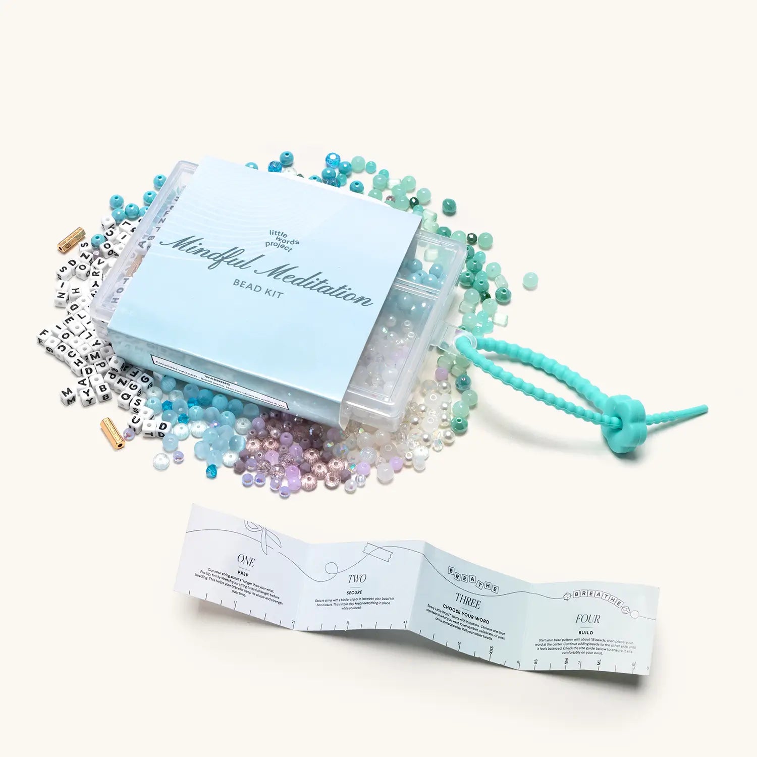 "Mindful Meditation" bead kit with scattered colourful beads, letter beads, teal cord, and an unfolded instruction booklet.