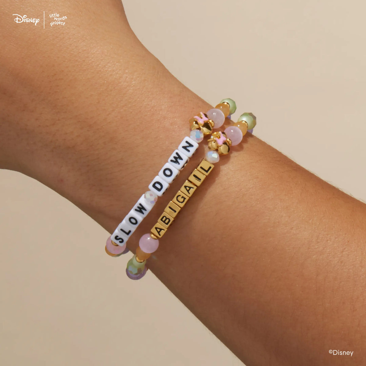 Minnie Custom Dot Darling Disney Mickey & Friends custom bracelets on wrist, one with white letter beads and one with gold letter beads, pastel beads and gold plated Minnie Mouse beads with pink bows