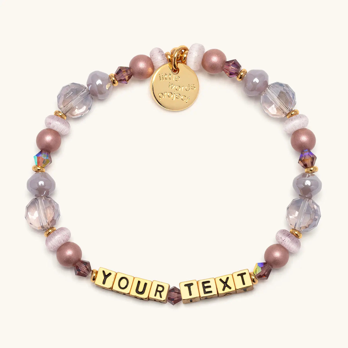 Custom Nice Spice bracelet in the Nice Spice bead pattern, gold letter beads reading Your Text, mauve pearl, lavender crystal, and clear faceted beads with gold accents, flat-lay on cream background