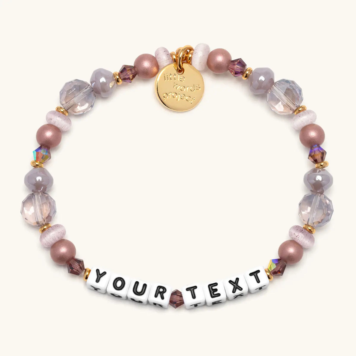 Custom Nice Spice bracelet in the Nice Spice bead pattern, white letter beads reading Your Text, mauve pearl, lavender crystal, and clear faceted beads with gold accents, flat-lay on cream background