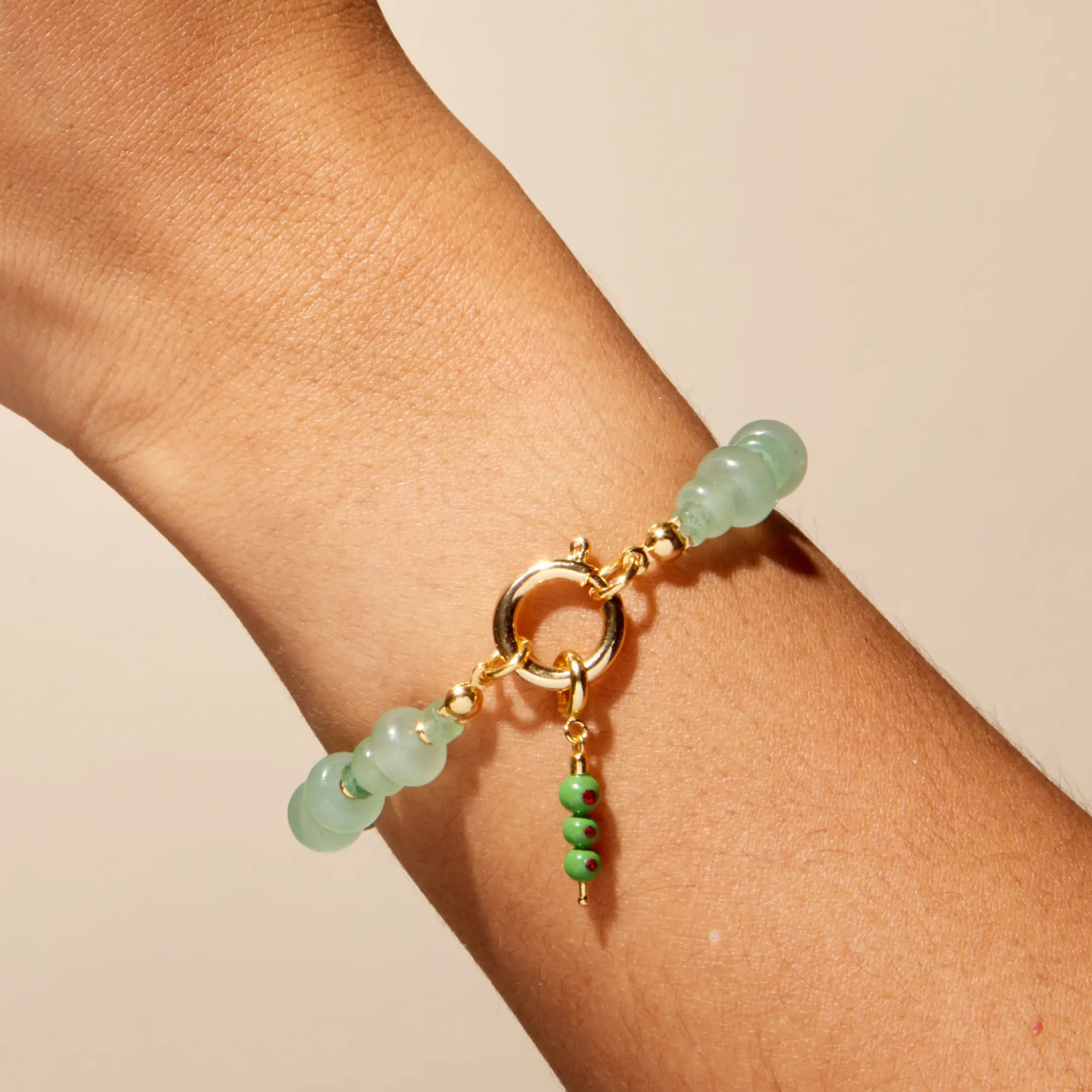 Green beaded bracelet with gold clasp on a wrist against a beige background