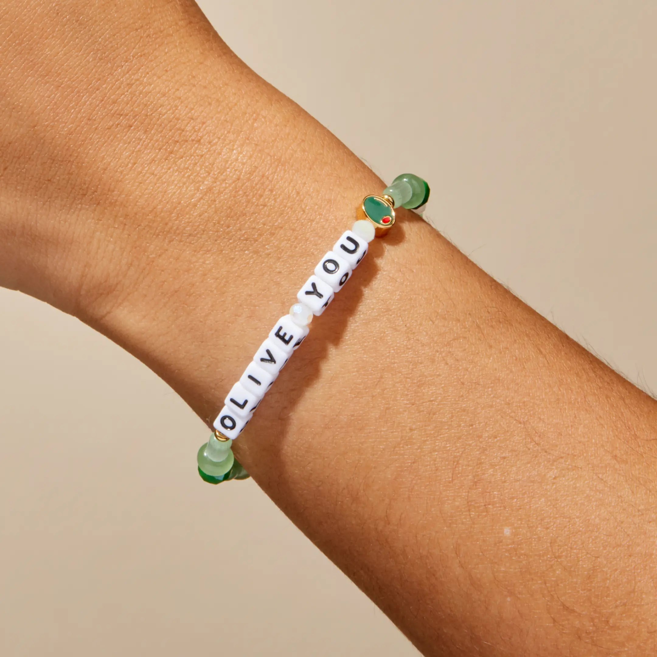 Bracelet with green beads and a message on a wrist against a neutral background