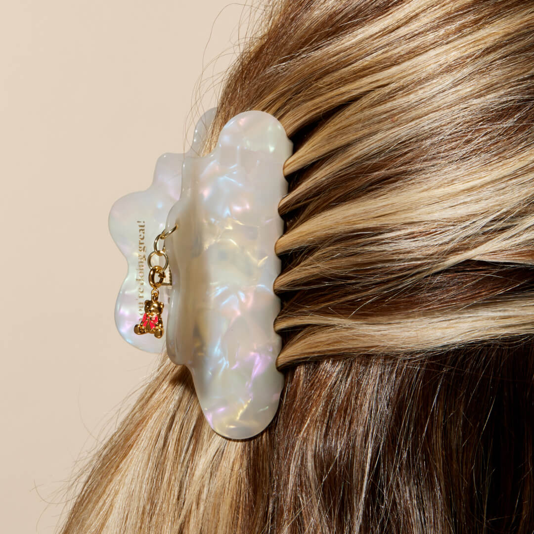 Iridescent hair claw with a small charm in blonde hair against a beige background