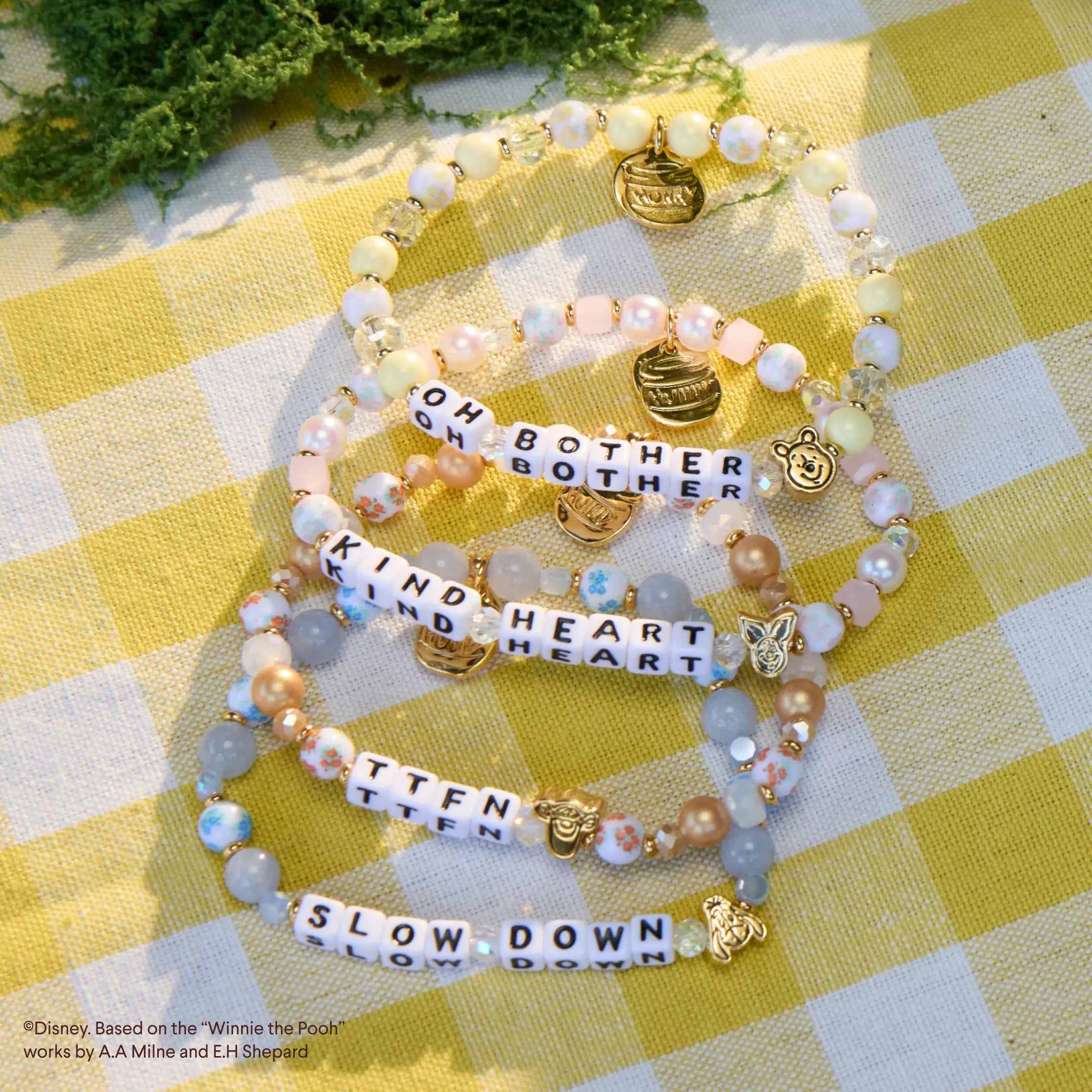 Stack of beaded bracelets with inspirational charms on a yellow checkered fabric background