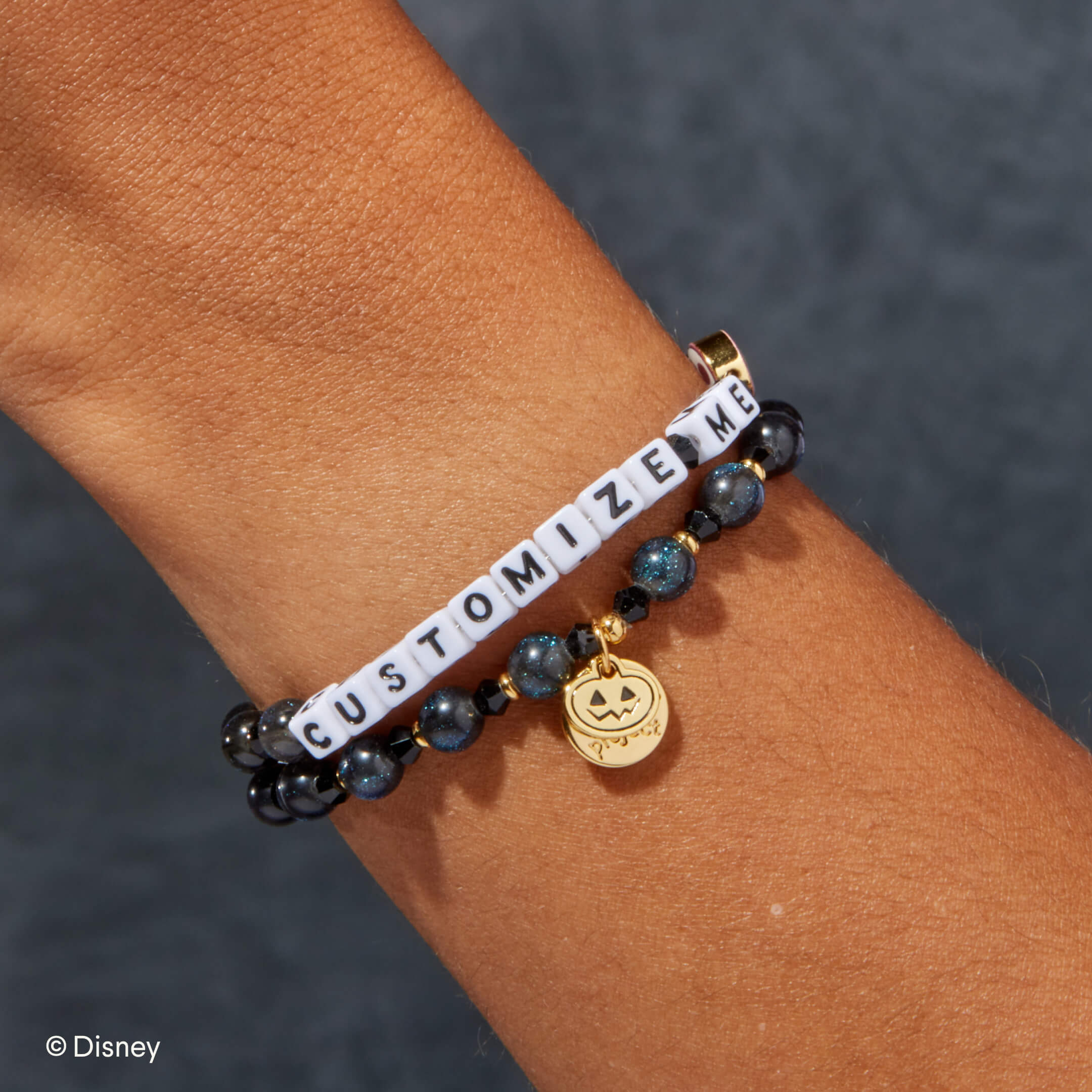 Bracelet with 'CUSTOMIZE ME' charm on a wrist against a dark background