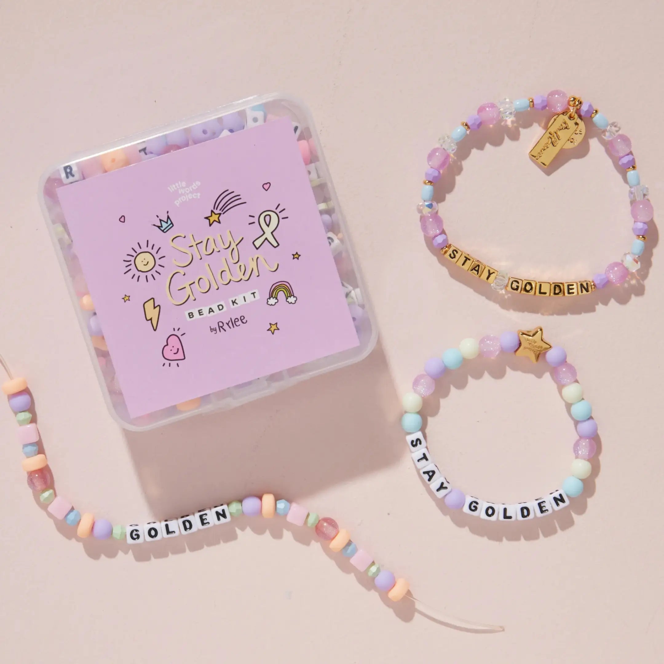 Stay Golden Bead Kit Set Rylee Ta styled with purple bead kit box, white letter bead bracelet and kids bracelet on a blush pink background