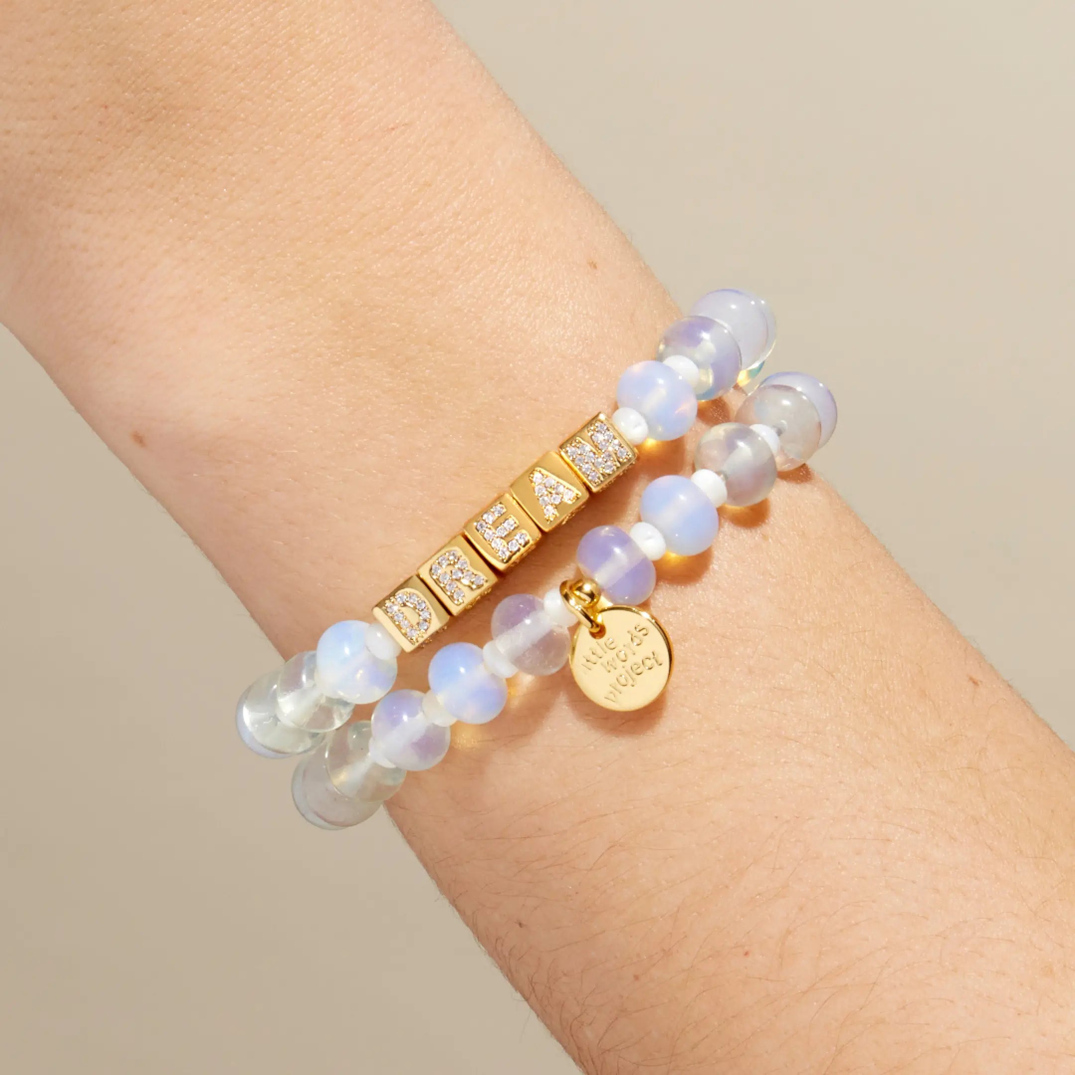 Two bracelets with gold accents on a wrist against a neutral background