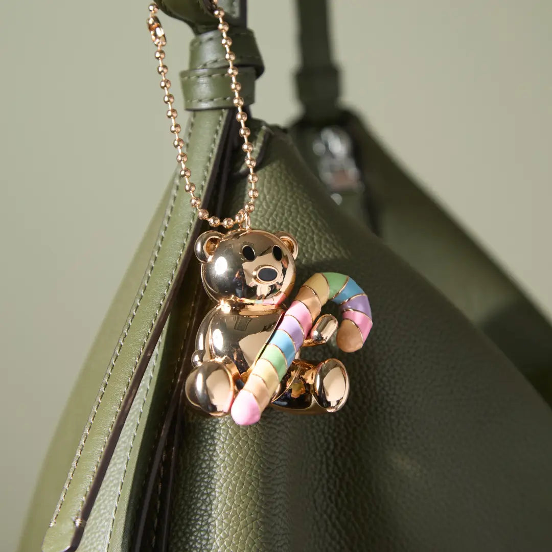 Gold teddy bear charm with a rainbow candy cane on a green bag.