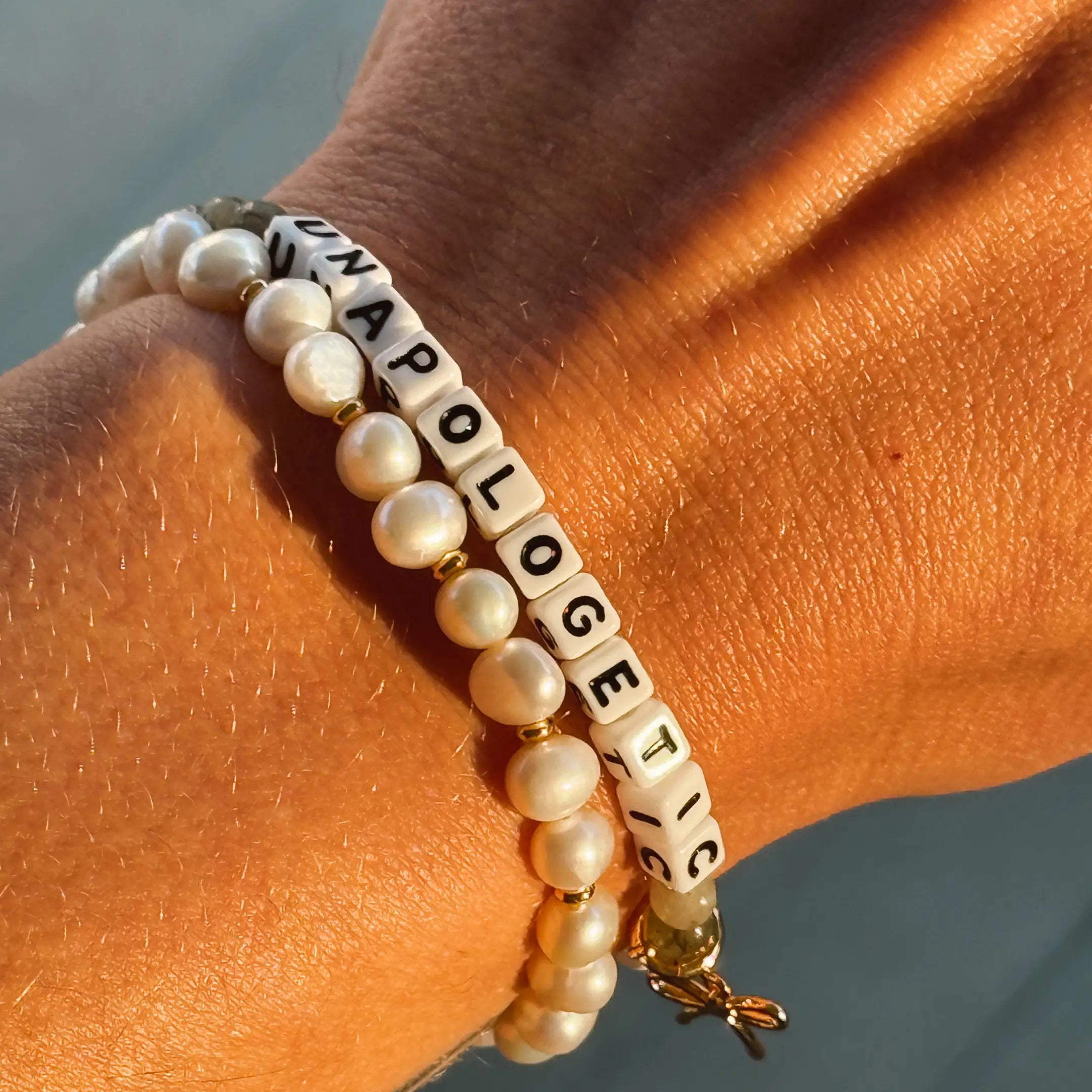 Bracelet with pearl beads and letter beads spelling 'UNAPOLOGETIC' on a wrist.