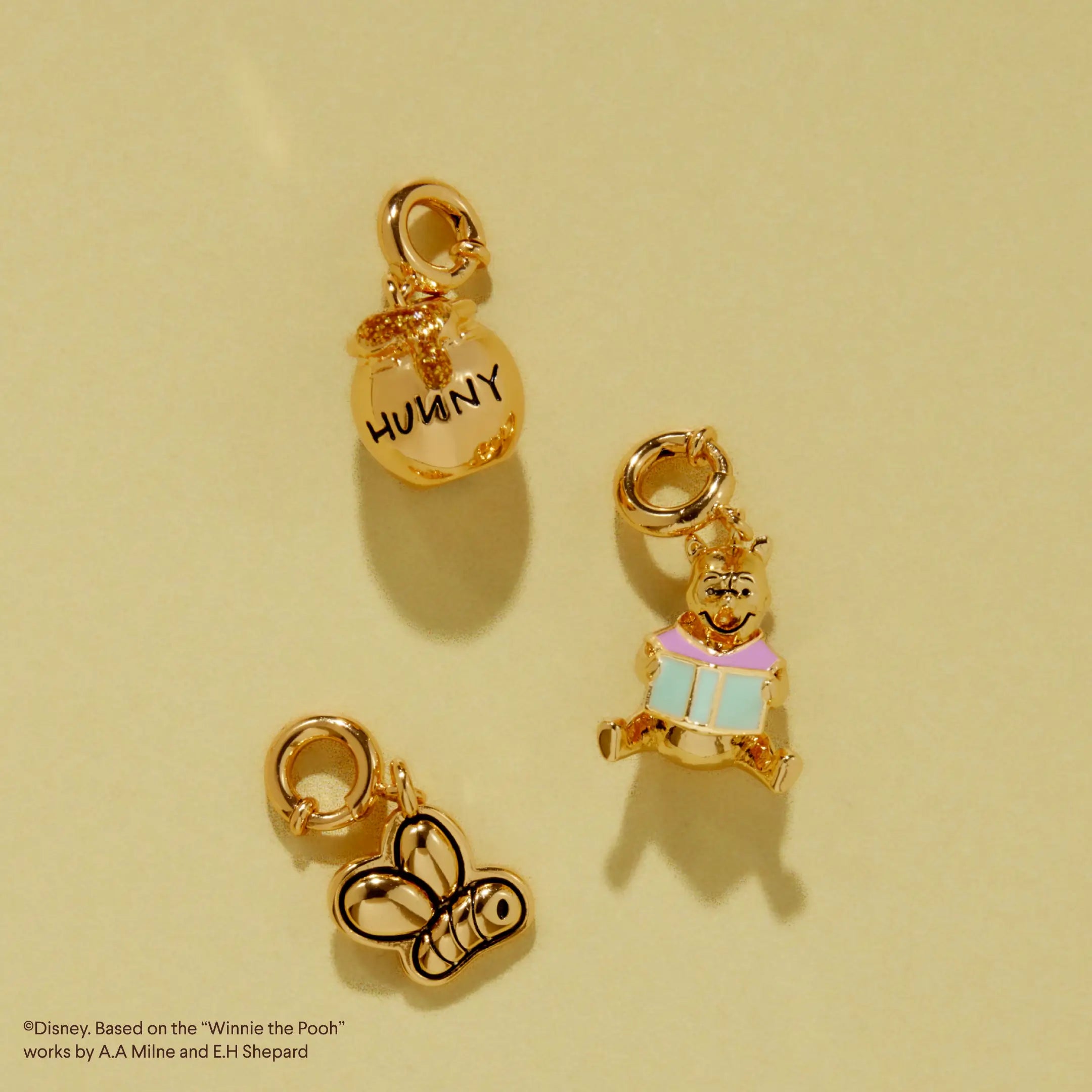 Three gold Winnie the Pooh charms on a beige background.