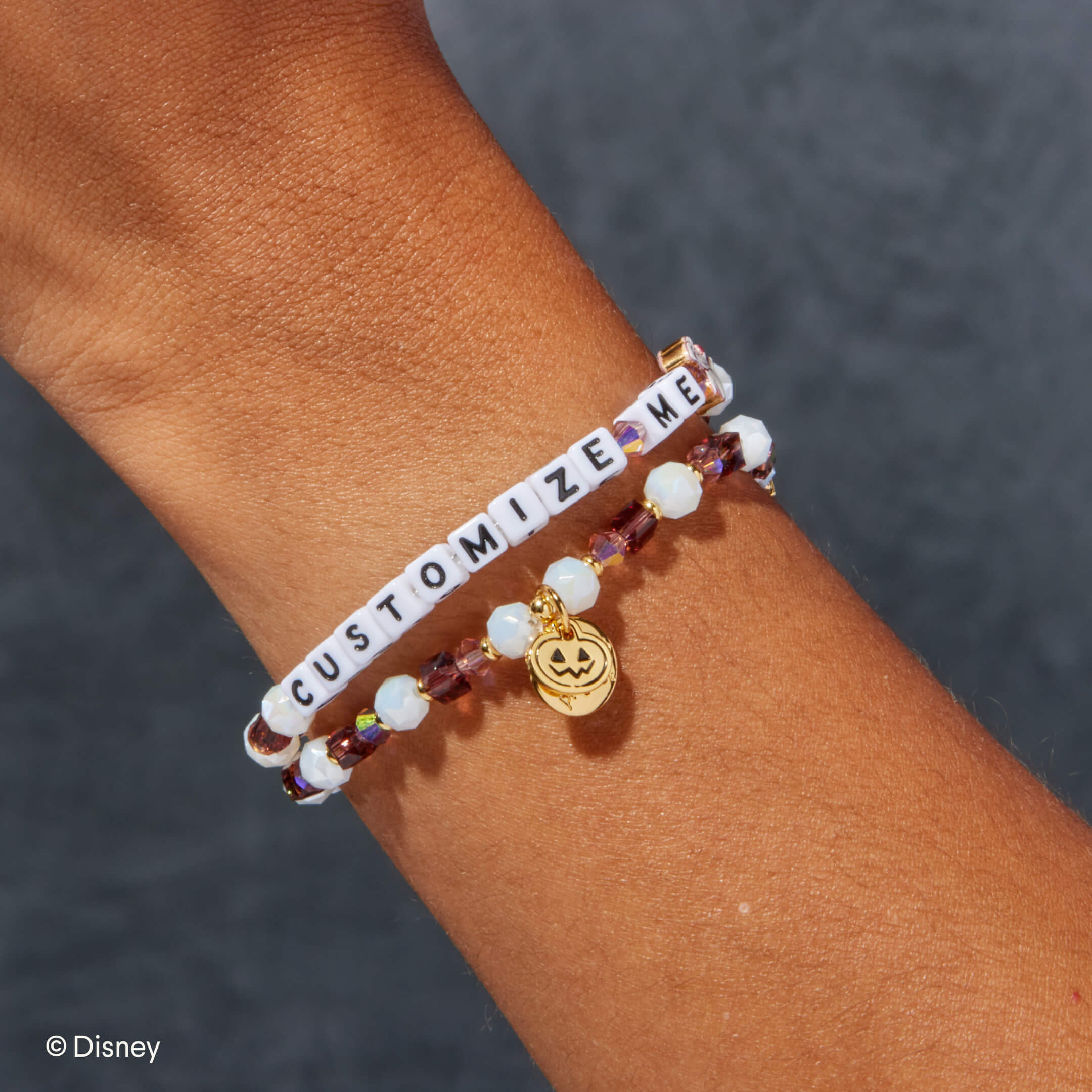 Bracelet with 'CUSTOMIZE ME' and pumpkin charm on wrist against a dark background