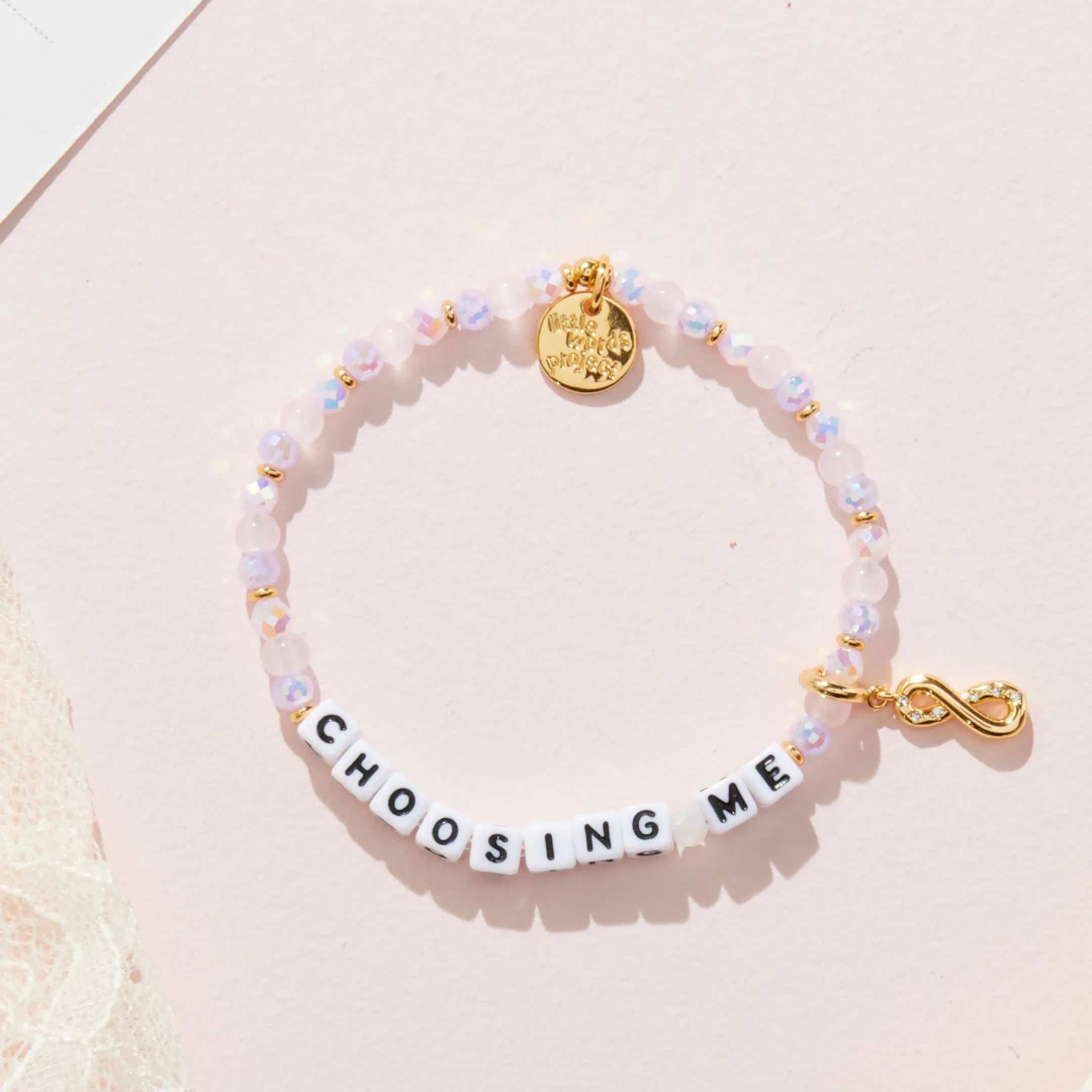 Bracelet with 'CHOOSING ME' charm on a light pink background