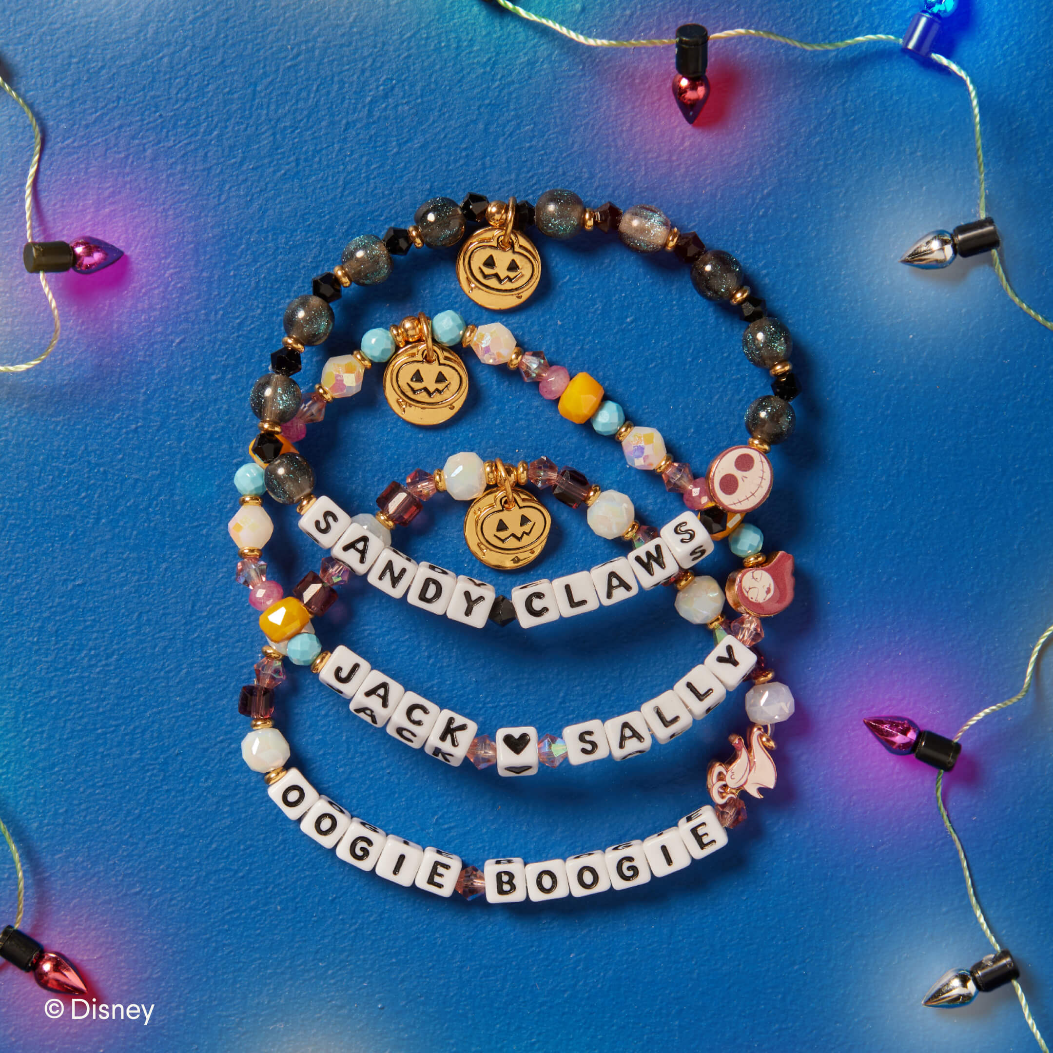 Three beaded bracelets with Halloween-themed charms on a blue background with string lights.