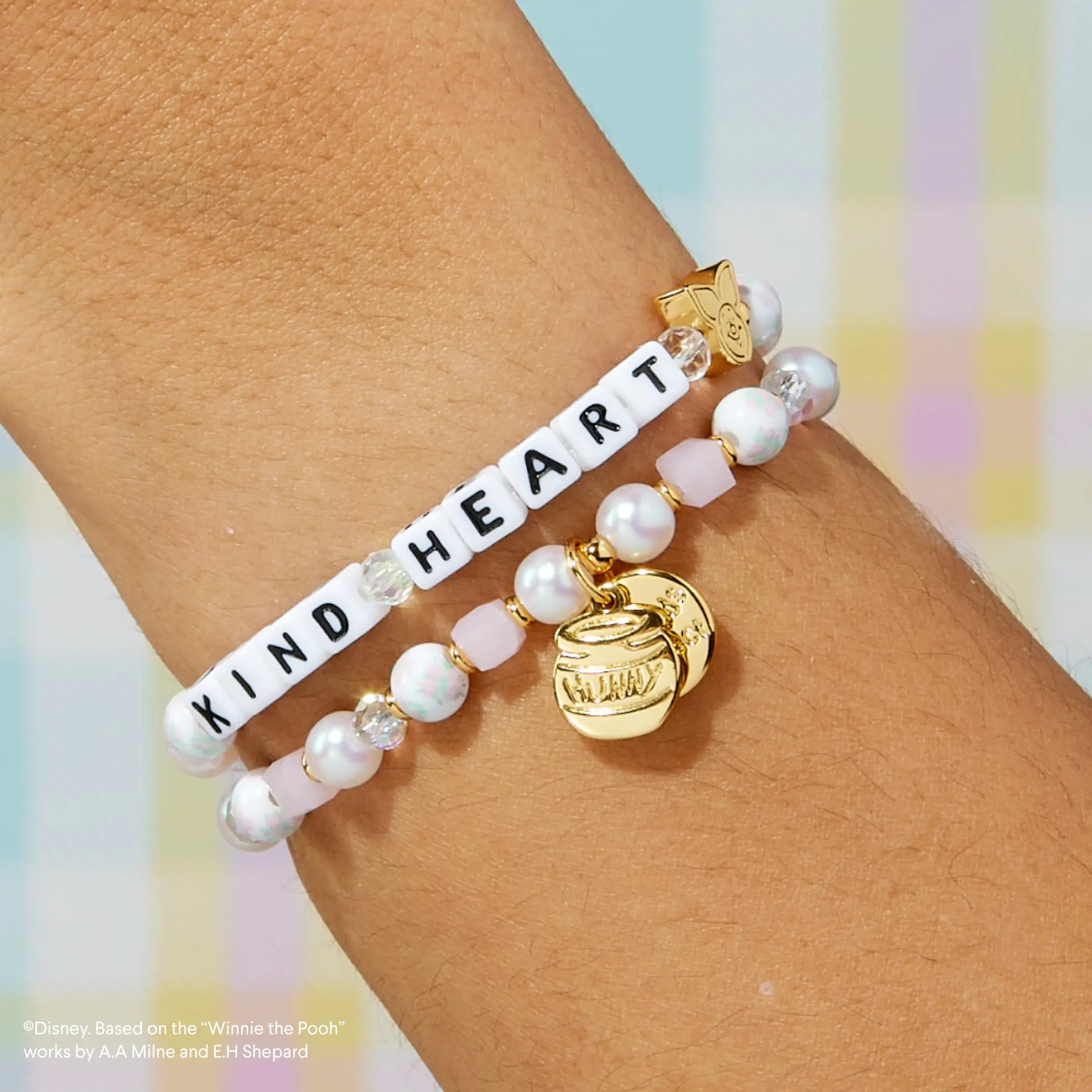 Bracelet with 'KIND HEART' on wrist against a pastel background