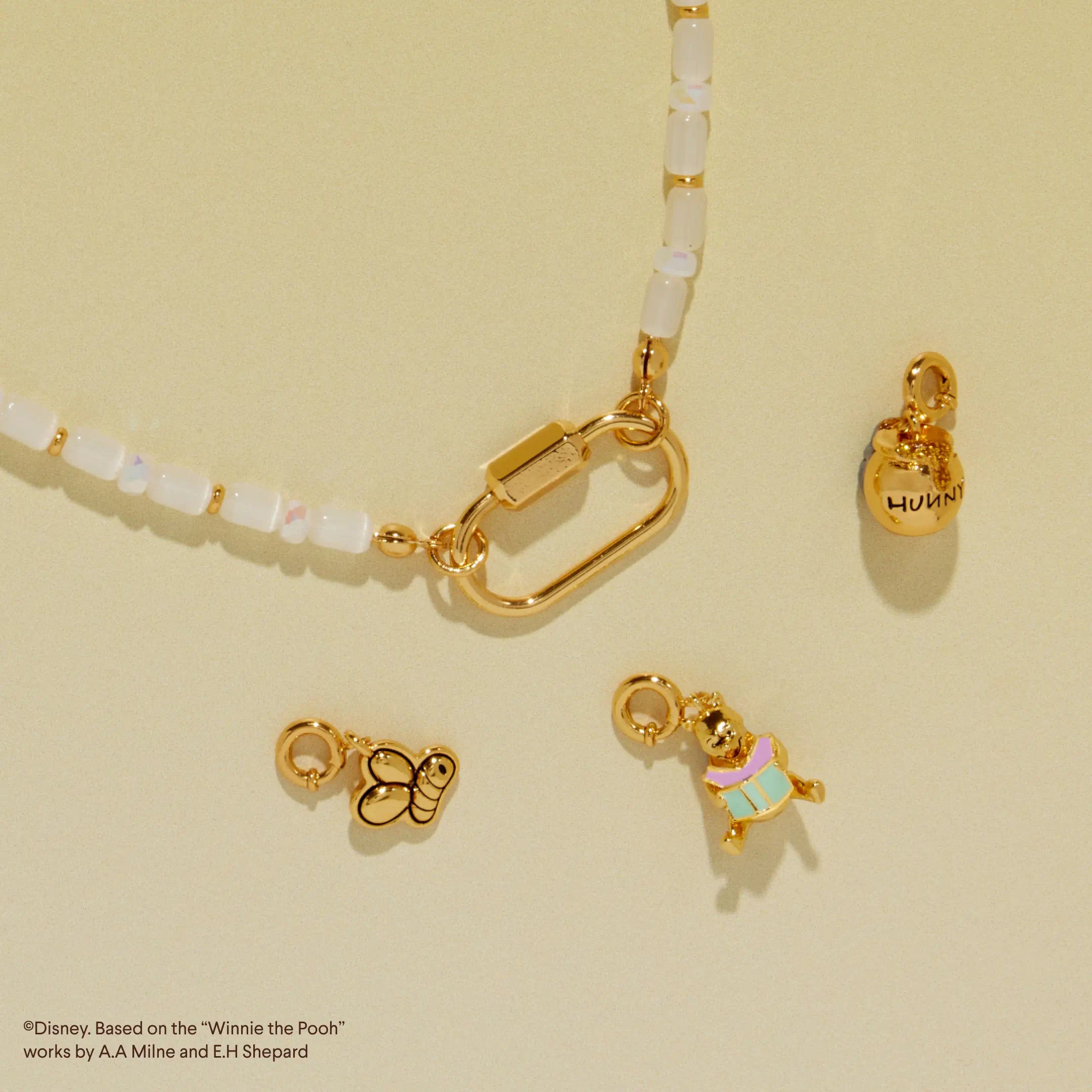 Gold charm necklace with various charms on a beige background