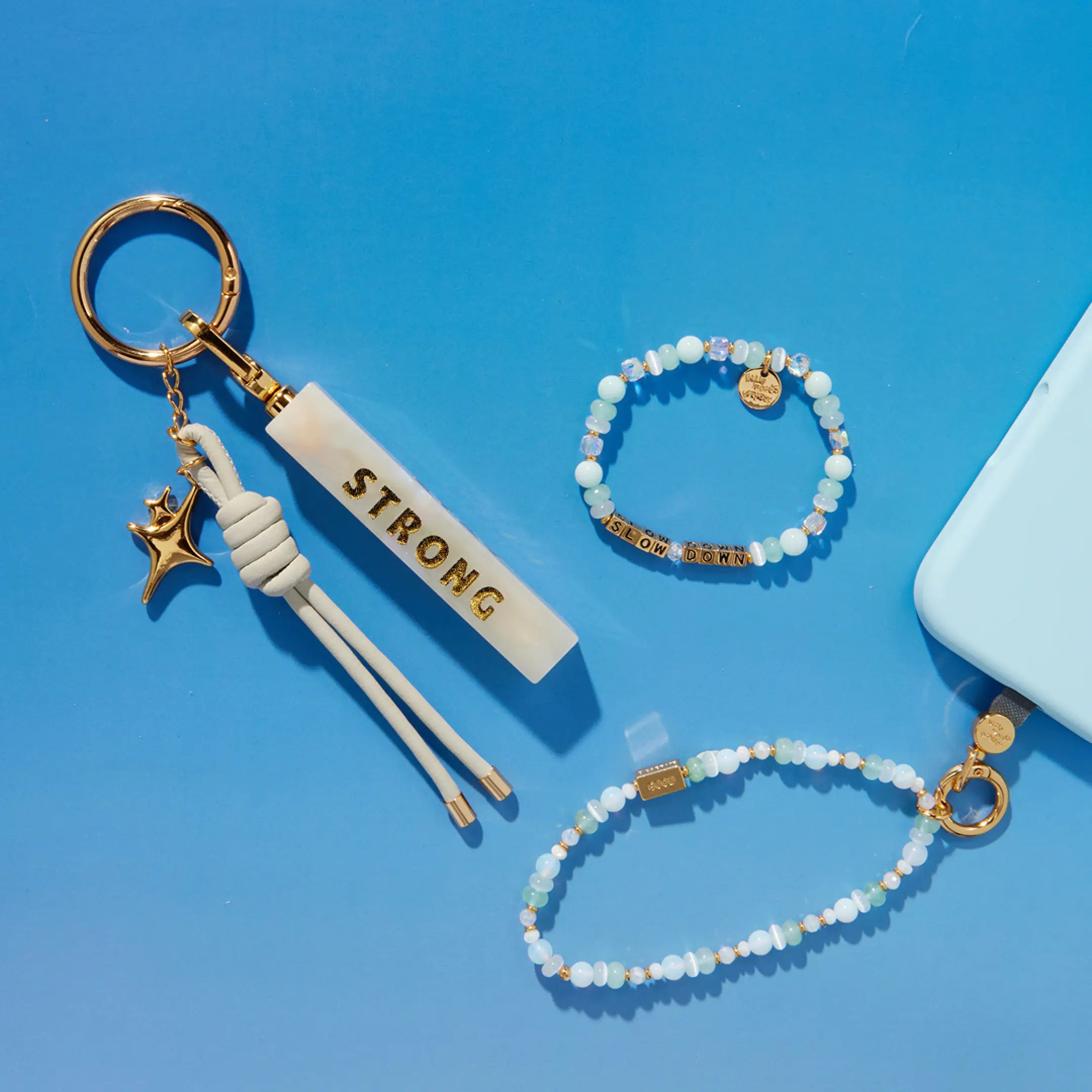 "Strong" keychain with star charm and tassel, a beaded bracelet, and a beaded phone strap in soft blue and gold tones.