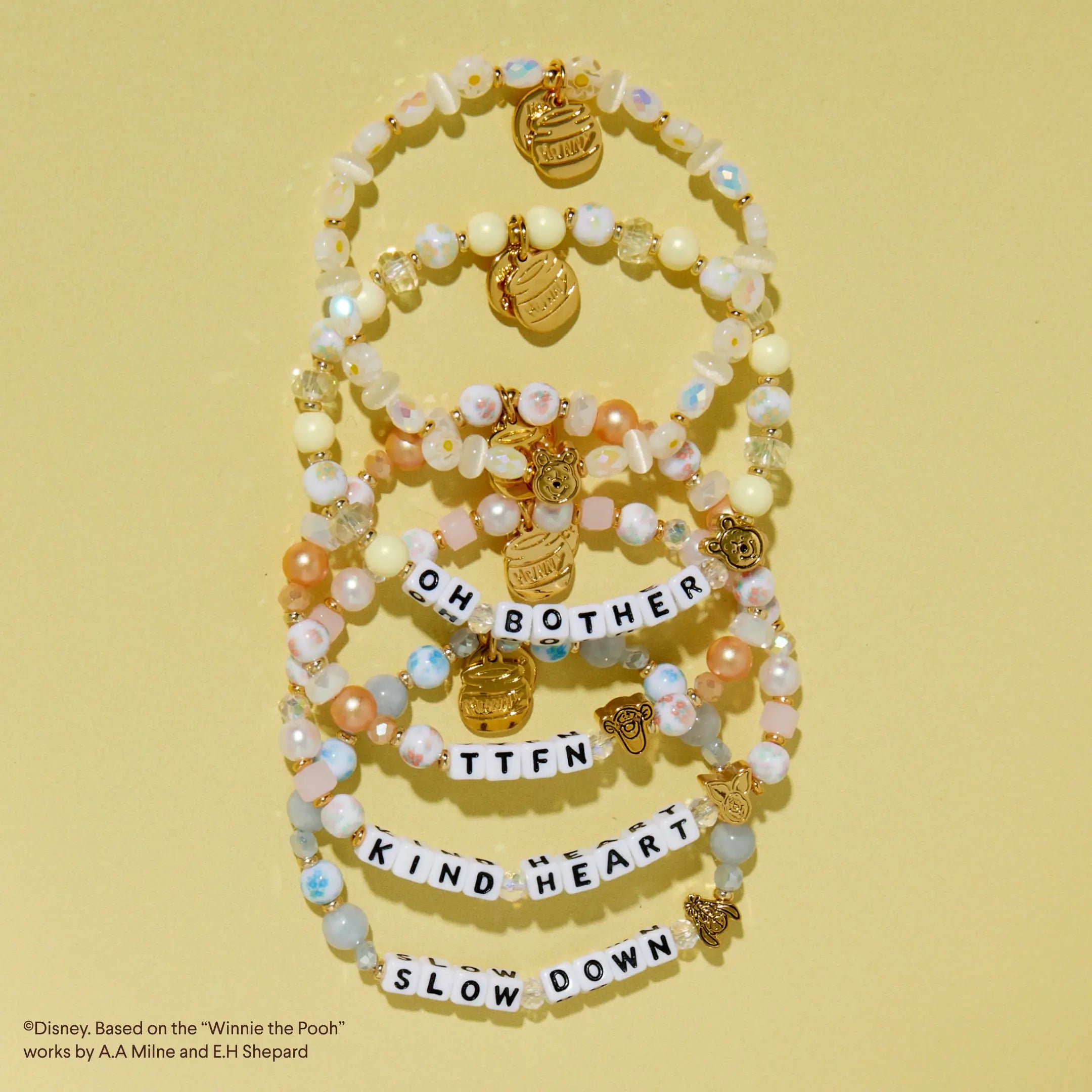 Stack of beaded bracelets with letter charms on a yellow background