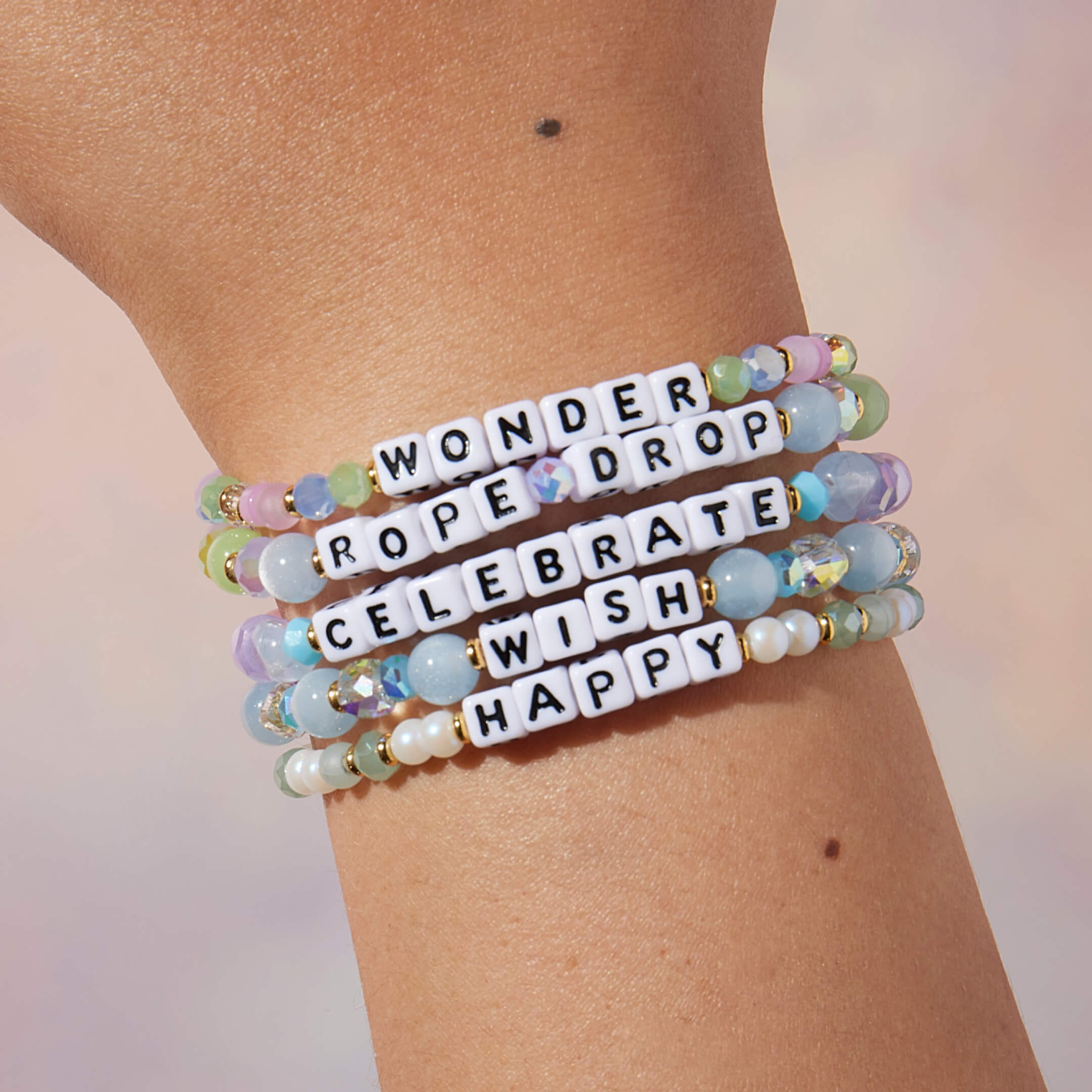 Stack of colorful beaded bracelets with inspirational words on a wrist against a neutral background