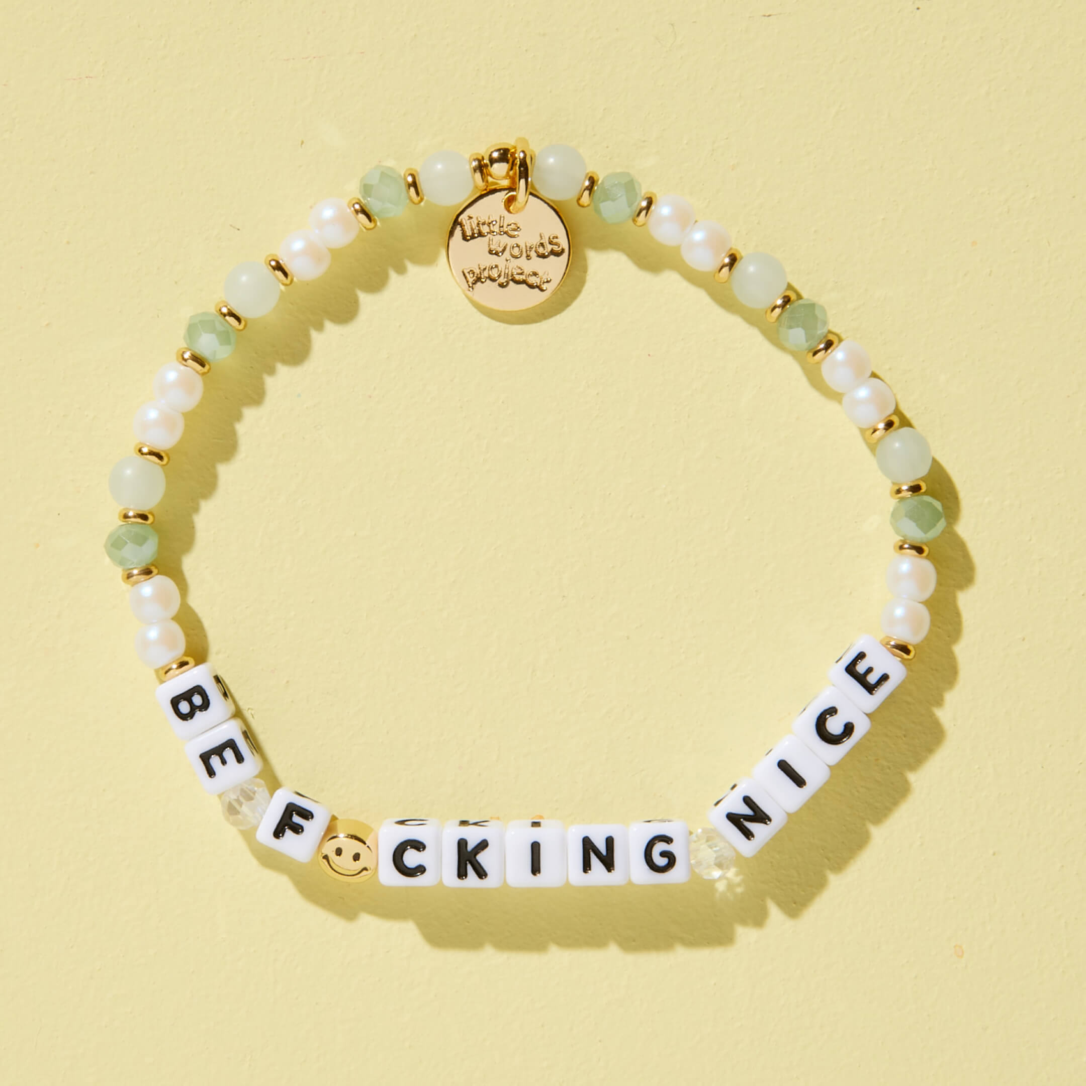 Bracelet with letter beads spelling 'BE F*CKING NICE' on a yellow background